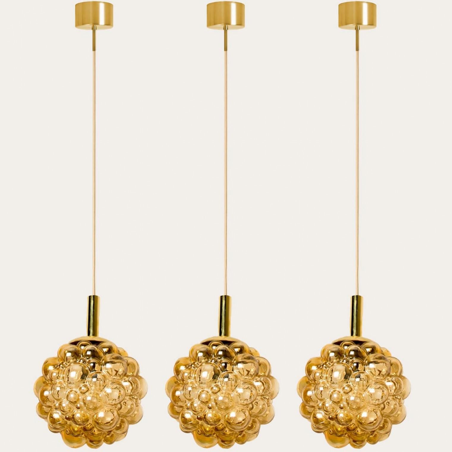 1 of the 3 beautiful pendant with bubbled glass by Helena Tynell, manufactured around the 1970s.

High-end hand blown amber glass which creates a stunning illumination in every interior.

The cable can be adjusted to alter the height