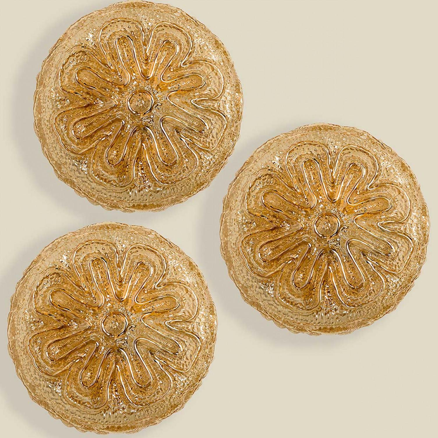 1 of the 3  textured amber glass wall lights designed in the style  of Helena Tynell around 1960-1970 in Europe, Germany. The rich texture is shaped like a flower and gives a wonderful glow. The round glass is mounted on a brass colored metal back