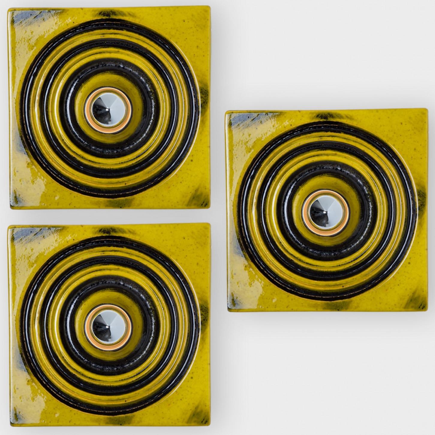 Beautiful square ceramic wall lights, manufactured in Germany around the 1970s.

The wall lights have a yellow glaze, the grooves and accents of the lamp are accentuated with a black glaze layer.

We used silver light bulbs (see images), but clear