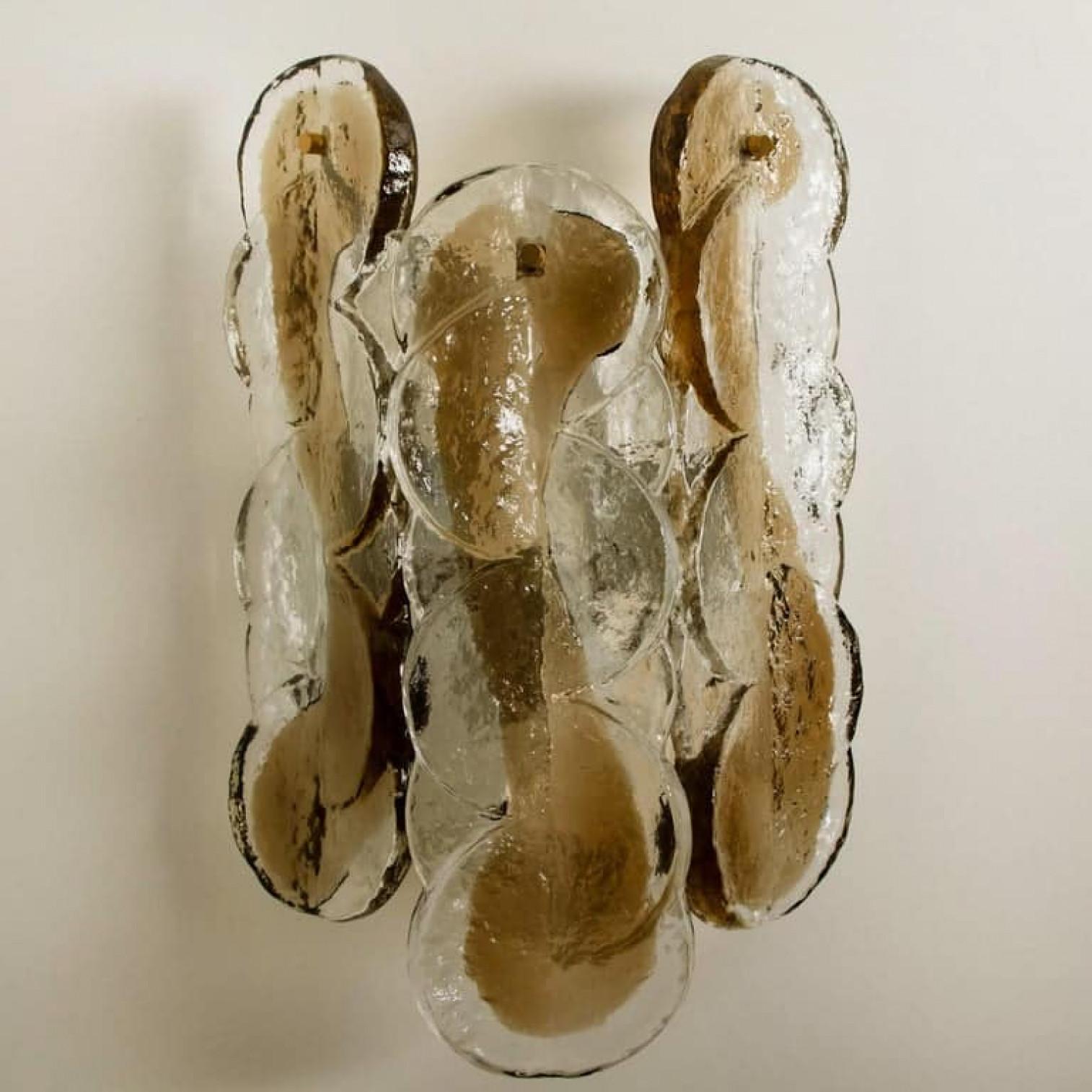 Coppia di appliques Kalmar swirl con leggero turbinio color oro-ambra. Il bellissimo e spesso vetro testurizzato è completato dalla ferramenta cromata. Design semplice e pulito. Vetro fuso soffiato a mano, realizzato in vetro fumé e trasparente.