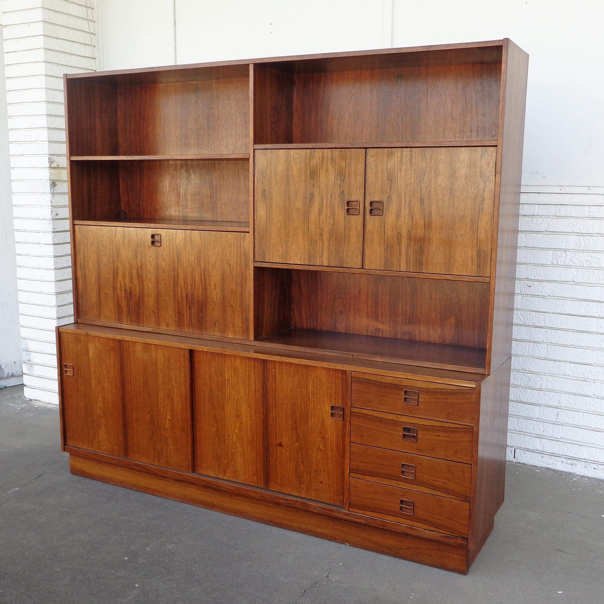 Rosewood bookcase wall unit by Poul Hundevad for Aerthoj Jensen and Molholm Herning 

Top unit has four green felt-lined drawers and a drop desk with an open shelf.
Six smaller shelves behind a two door section. Bottom unit has two sliding door