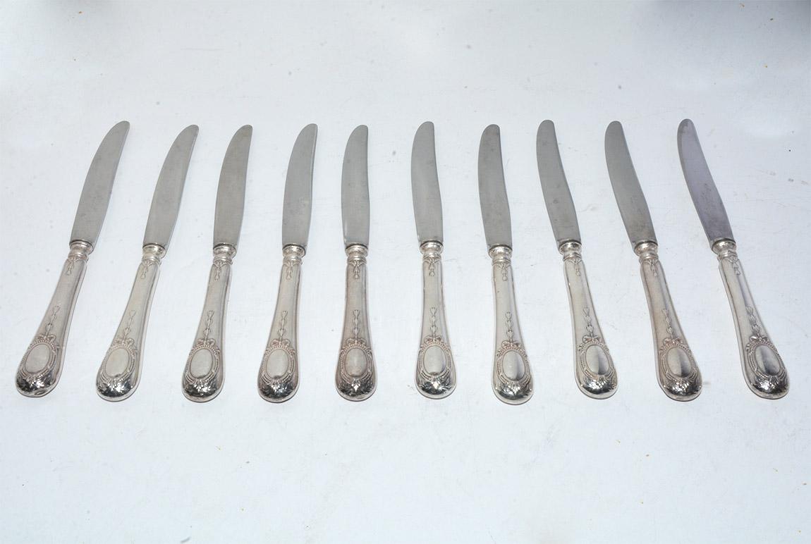 The 10 lunch-size knives with neoclassical motifs have antique silver plated handles and new stainless steel blades. The handles are continental silver plate. The blades have these engraved initials:: S.F.A.M. and INOX. The handles are engraved with