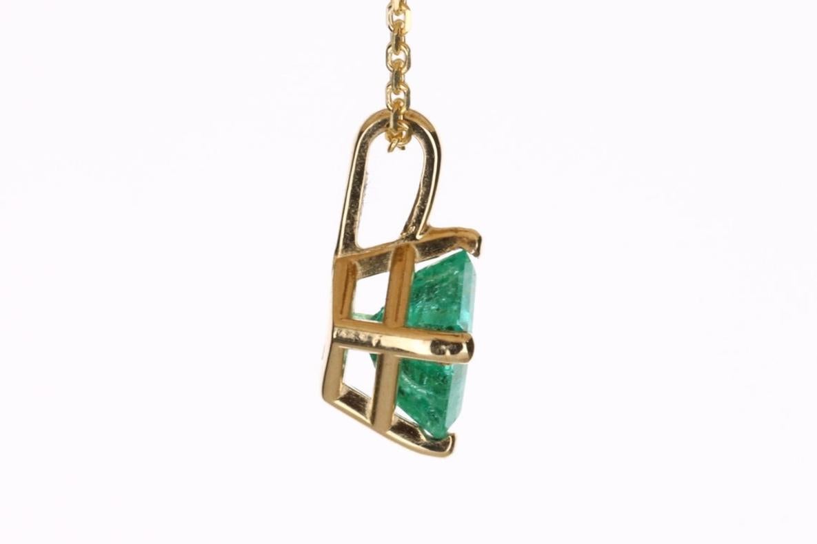 Displayed is a classic Colombian emerald solitaire necklace set in 14K yellow gold. This gorgeous solitaire pendant carries a full 1.0-carat emerald in a four-prong setting. Fully faceted, this gemstone showcases excellent shine. The gem has a