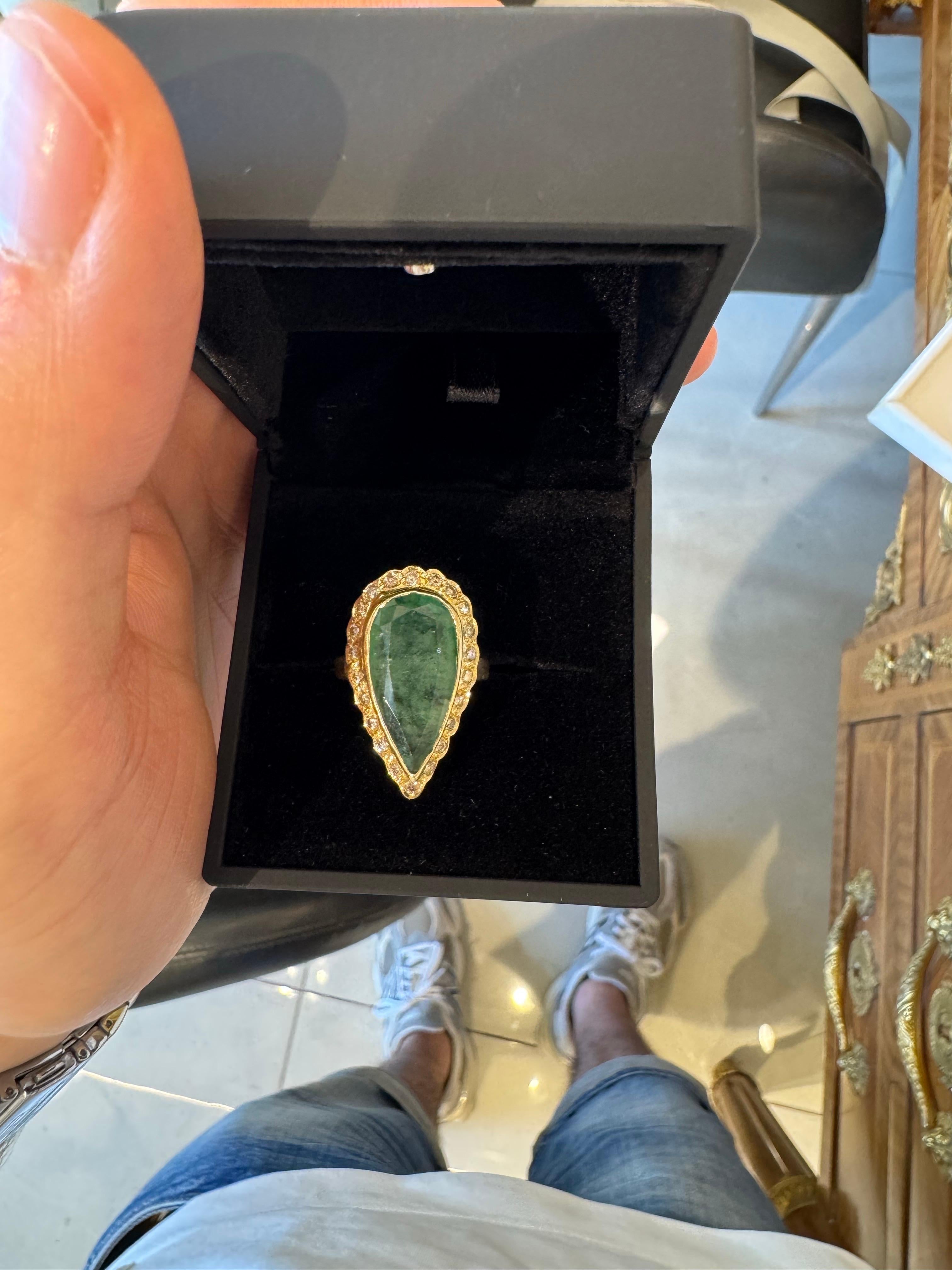 Dieser atemberaubende Ring besteht aus einem 10-karätigen birnenförmigen Smaragd, der in 14-karätigem Gelbgold gefasst und von einem zarten Halo aus 0,60 Karat F VS1 Diamanten umgeben ist. Das satte Grün des Smaragds kontrastiert wunderschön mit dem