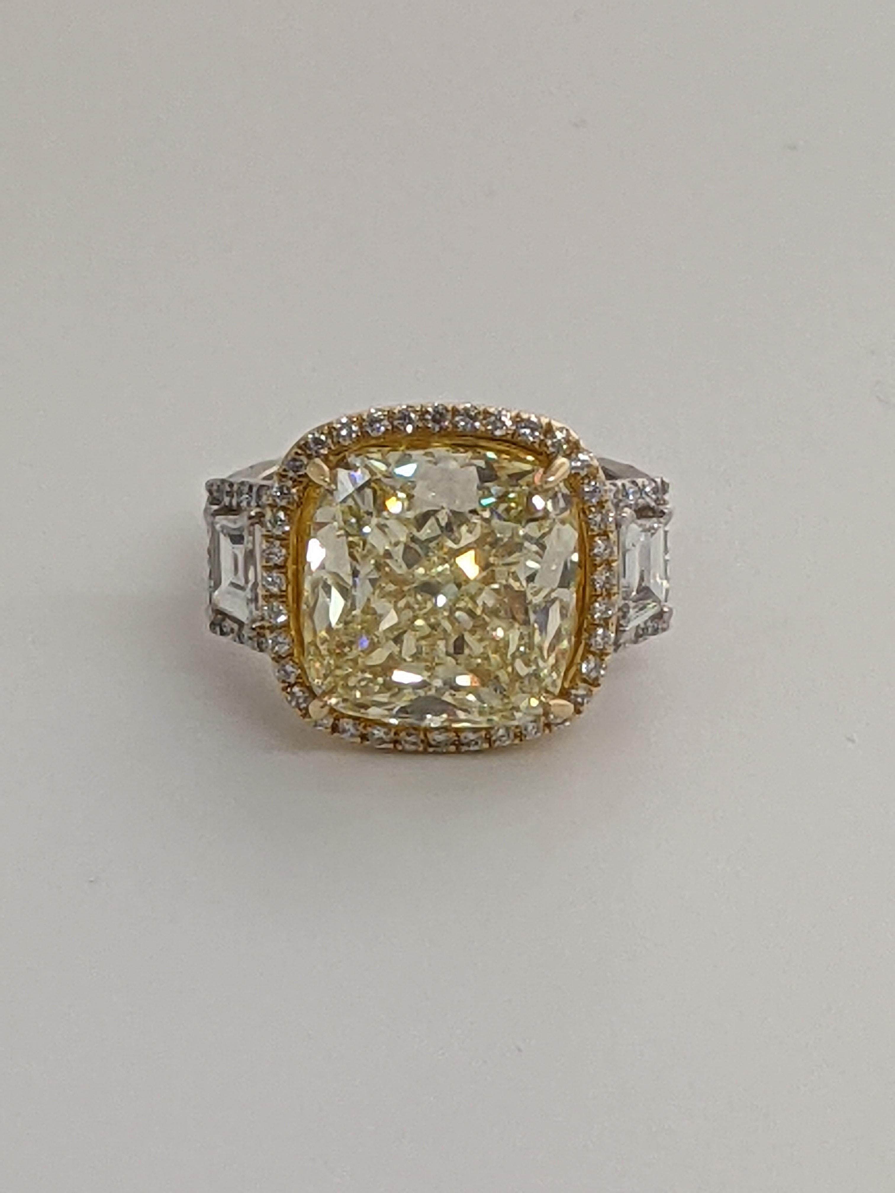 This gorgeous, statement making ring features a 10.20 Fancy Light Yellow cushion cut diamond of VS1 clarity as detailed with the GIA report.   On each side of the diamond are step cut white diamonds with a halo of smaller white diamonds.  GIA Report