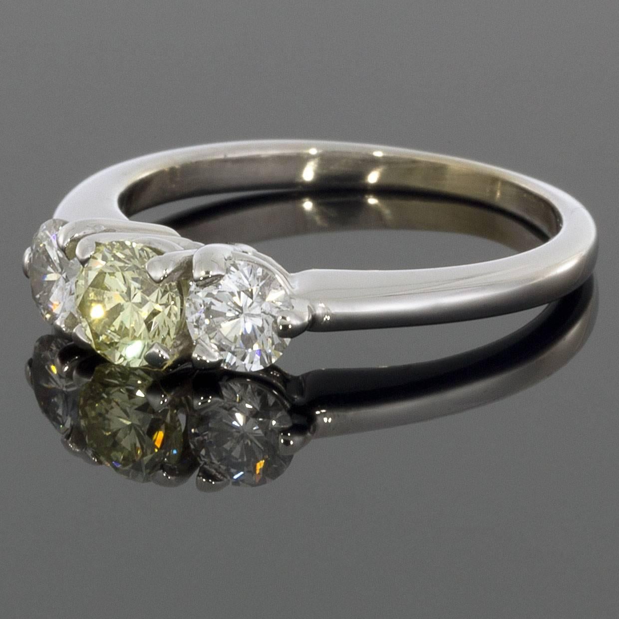 This gorgeous three-stone engagement ring features a stunning fancy light yellow round diamond. The center diamond is flanked by two white round diamonds. The diamonds grade as VS2 in clarity. The total carat weight of this ring is 1.0 carats. The