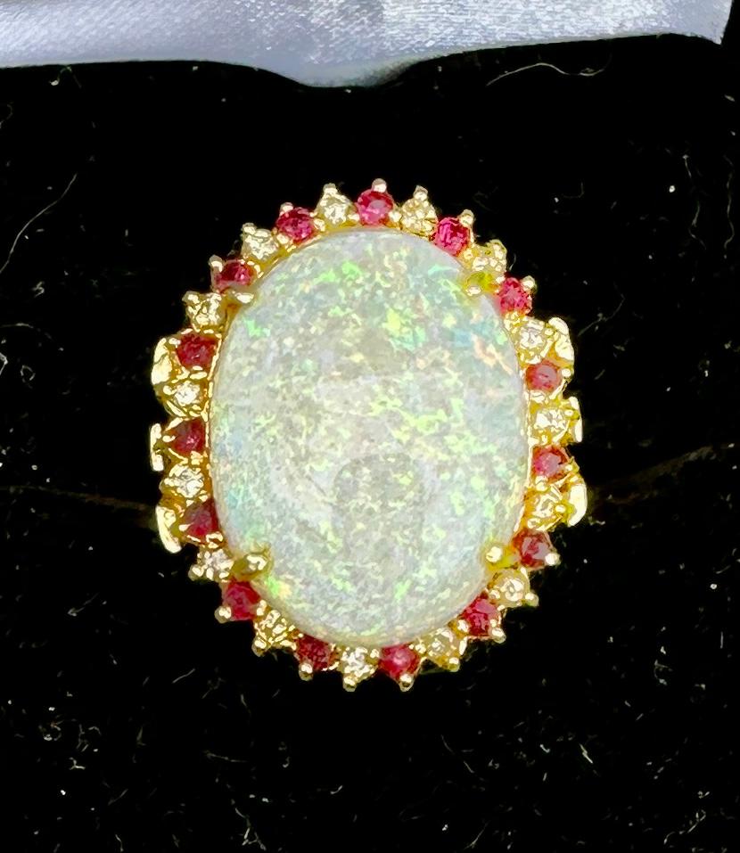 This is a stunning Retro - Hollywood Regency Ring with a gorgeous central 9.57 Carat Opal surrounded by a halo of 30 absolutely radiant Rubies and Diamonds in 14 Karat Gold.  The magnificent monumental oval opal cabochon gem is 21 mm by 16 mm by 5mm