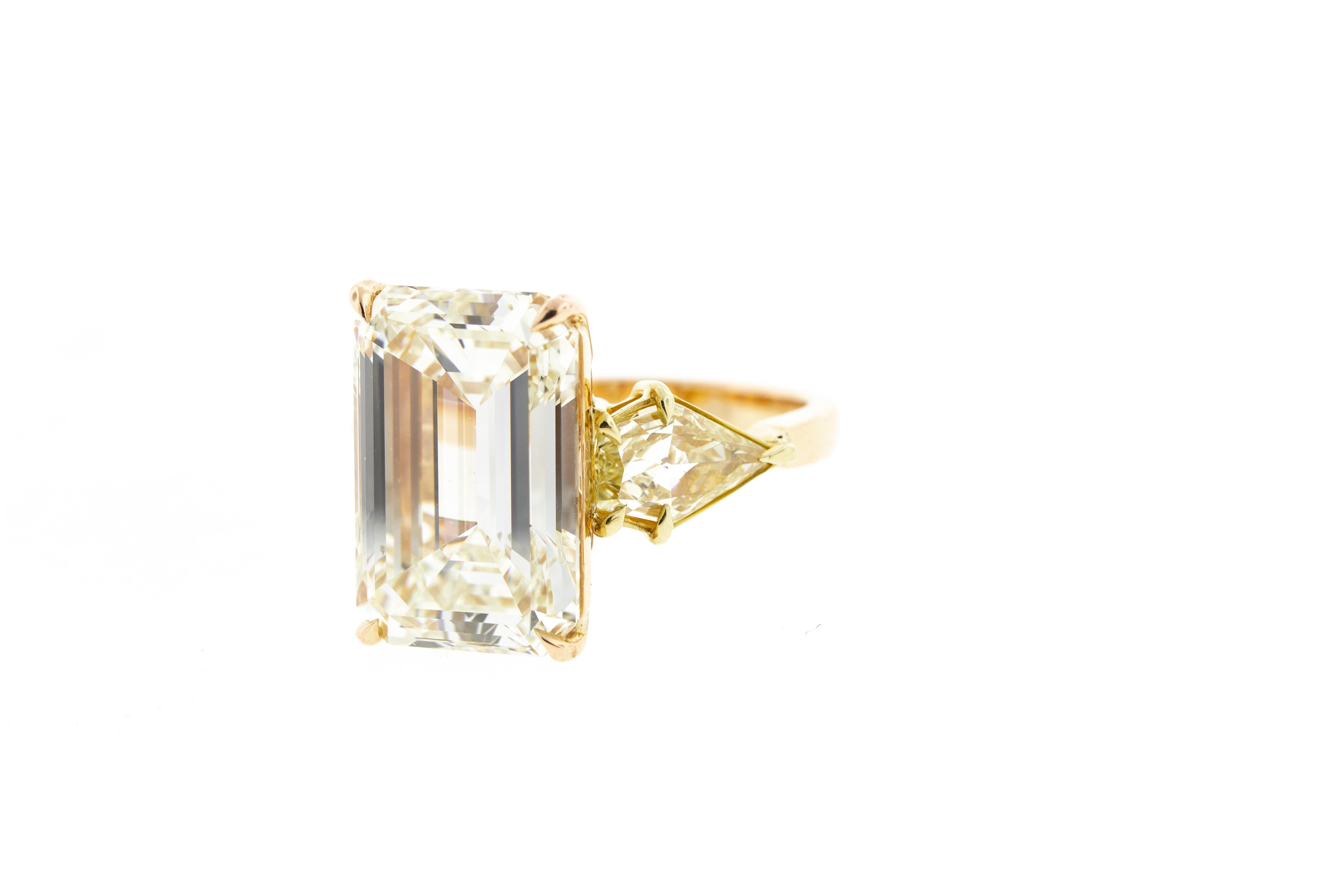 This vintage diamond ring features a 10 carat emerald cut center stone with a pair of fancy yellow kite cut side stones for a total carat weight of 11.37 and is set in two tone gold (rose and yellow) with delicate detailing under the basket.