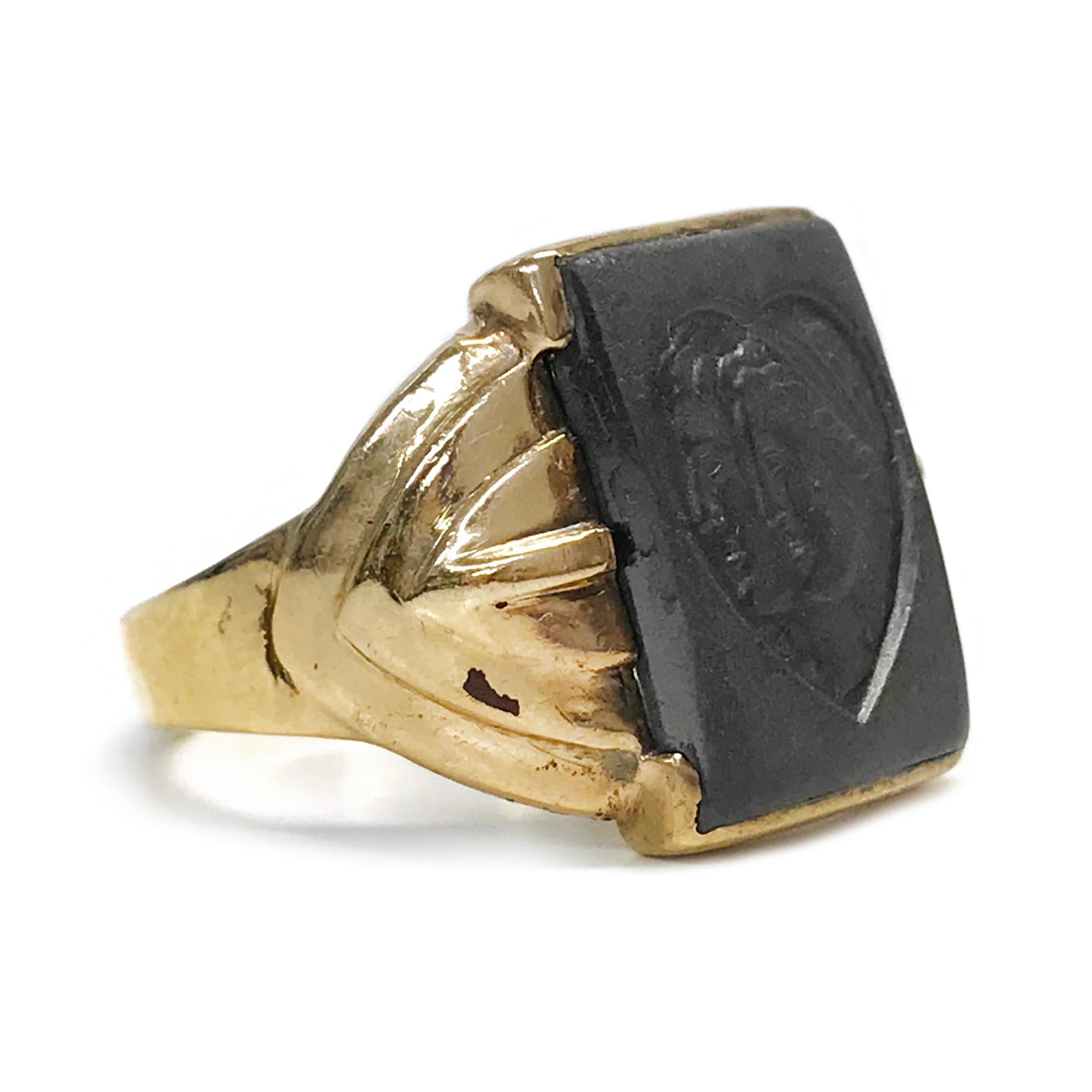 10 Karat Art Deco Hematite Intaglio Ring. The wide-band has an Art Deco motif and a smooth shiny finish. The center of the ring is a 15.86mm x 11.92mm Hematite Intaglio with a heart and a Roman couple. Stamped on the inside of the band is 10K. The