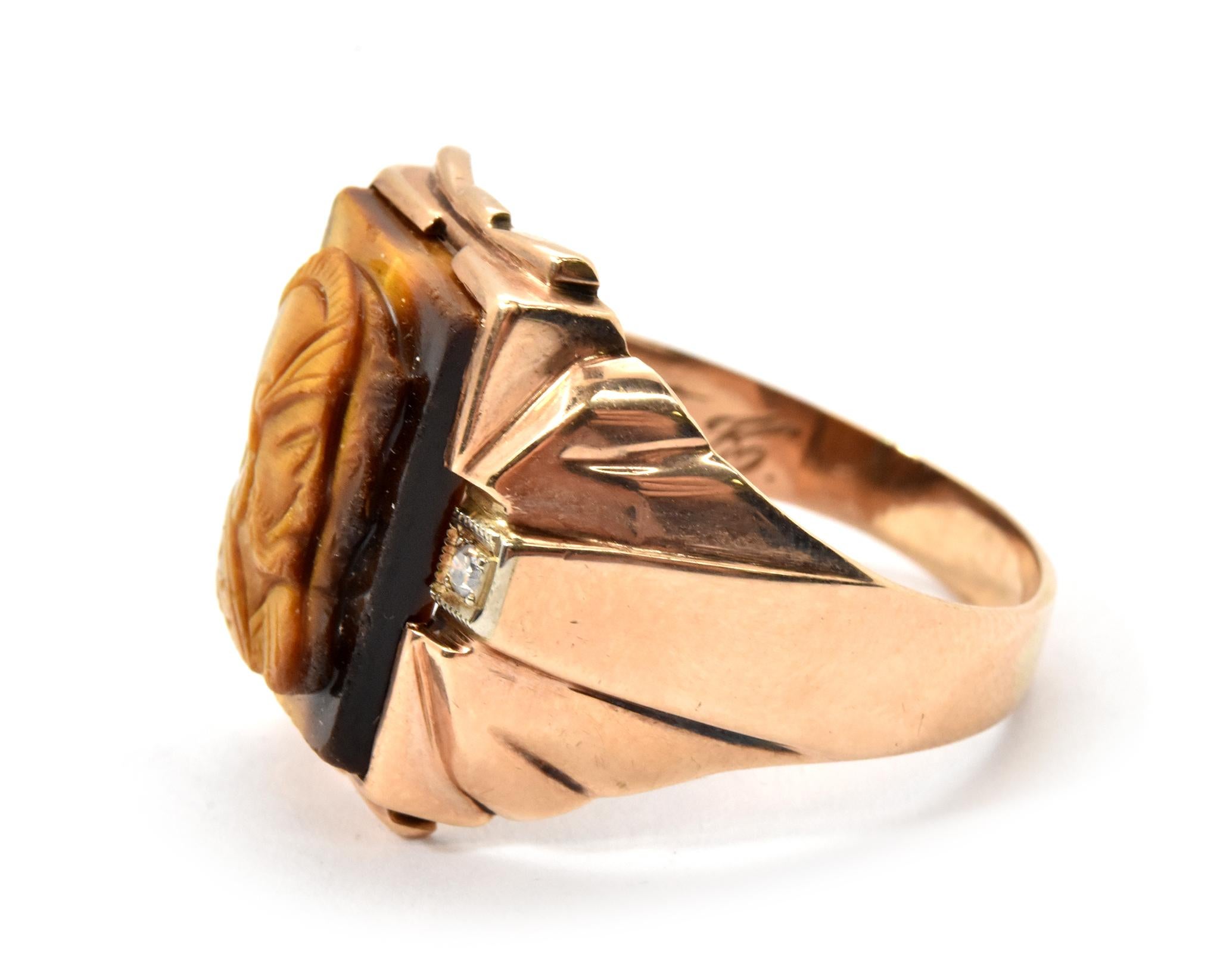This ring is made in 10k yellow gold, and it holds a carved tiger's eye stone. The carving features two men soldier's silhouettes. The ring measures 19.5mm wide and it weighs 7.3 grams. The ring is a size 12.5.