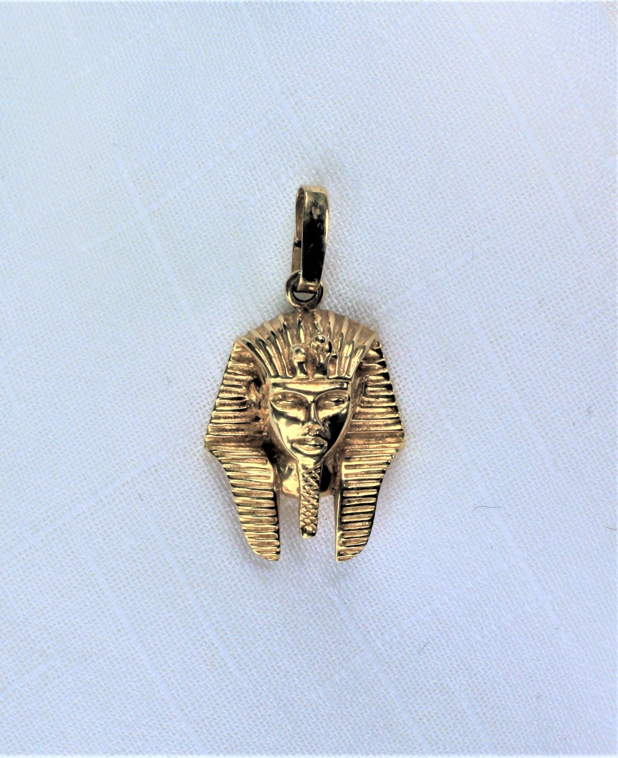 Made of solid 10 karat yellow gold, this figural pendant of the Ancient Egyptian Pharaoh Tutankhamun's iconic 'death mask't was done during the late 20th Century in the style of the Egyptian Revival movement. The pendant is quite detailed as