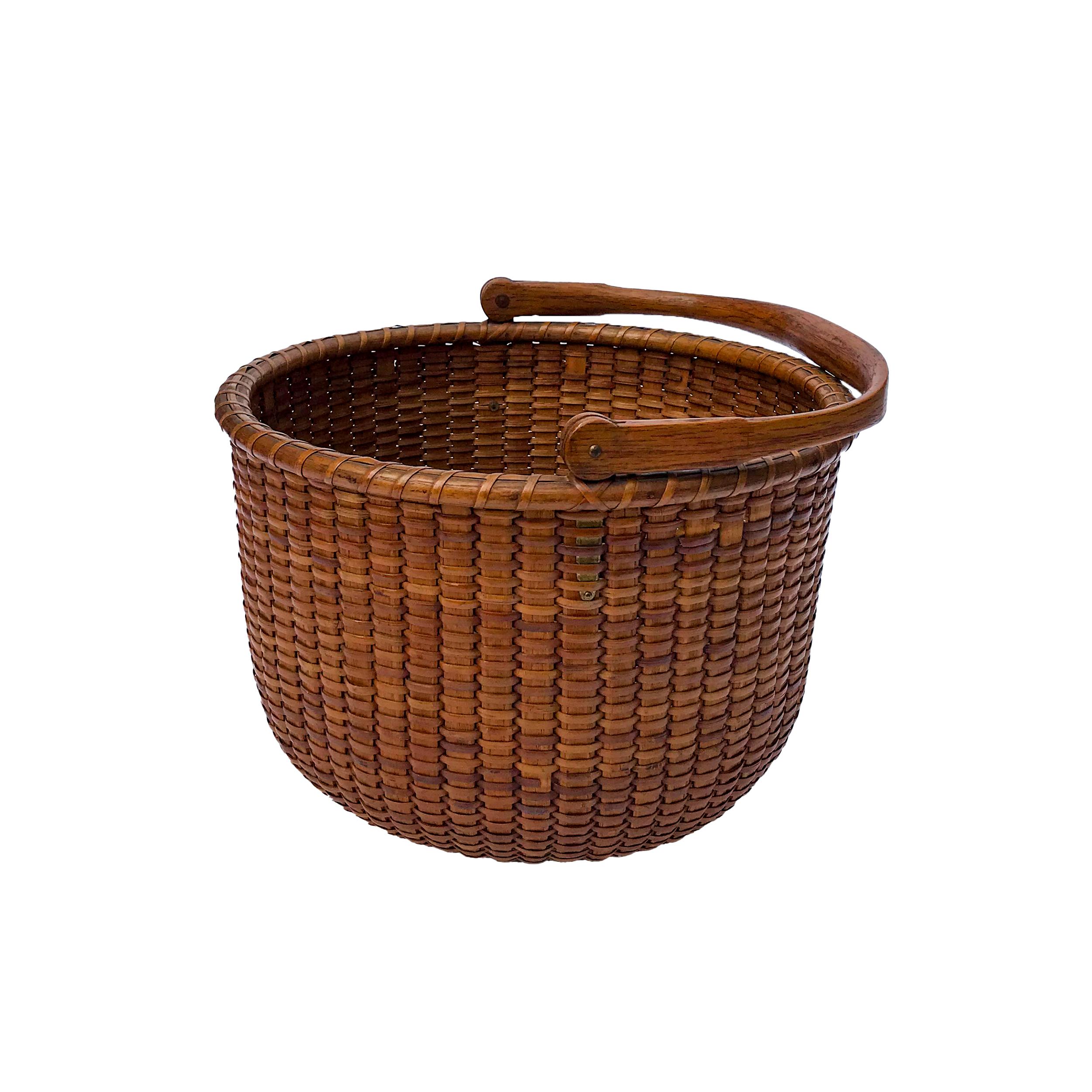 The basket has a rich honey patina throughout, made with oak staves and a swing handle that's notched and rounded at the ends and attached with brass ears. The mahogany bottom has four concentric rings which are typical features of an Andrew