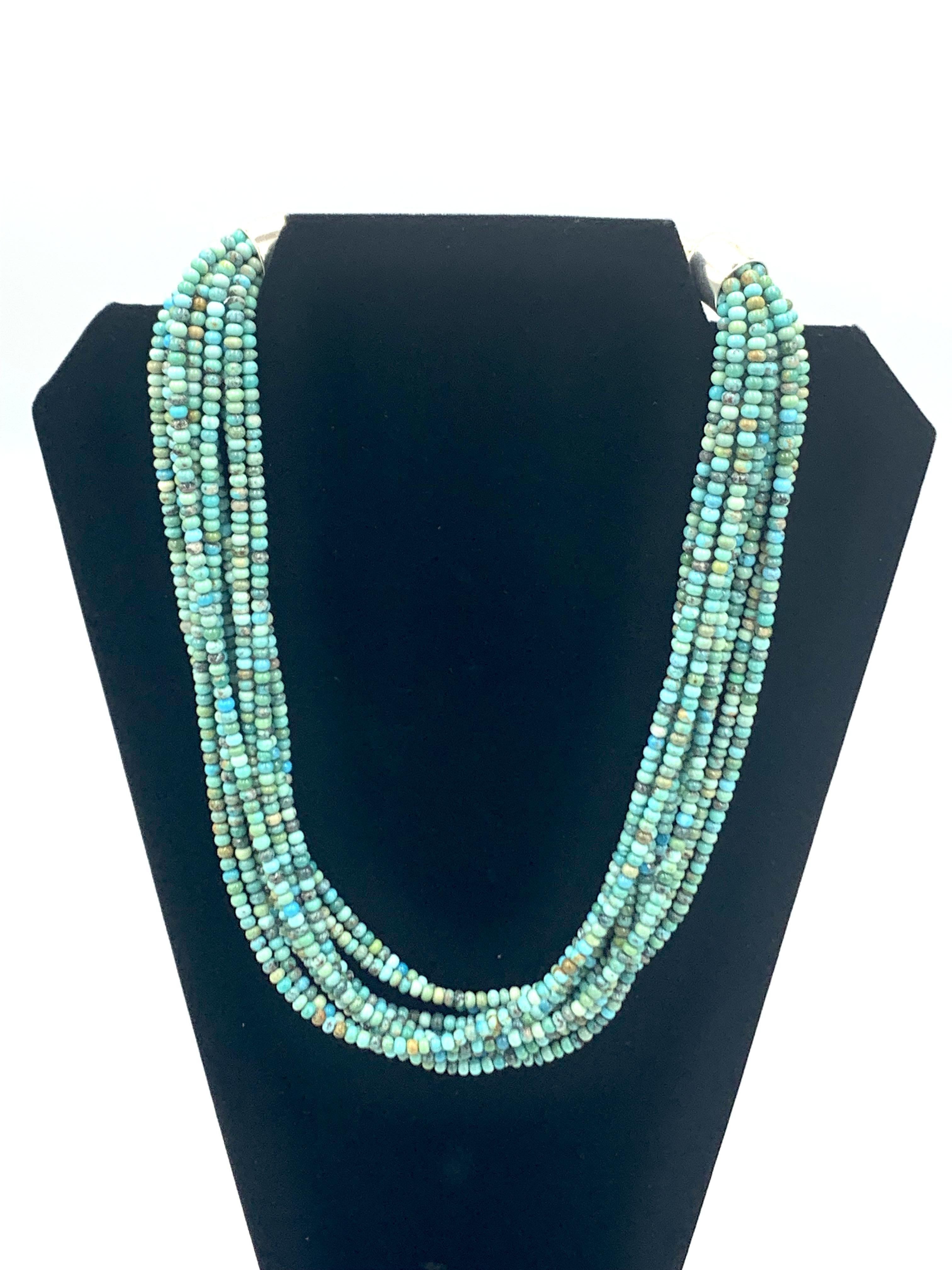 Questa elegante collana presenta dieci fili di perline di turchese Nevada arrotolate a mano, ciascuna modellata con cura per mostrare la bellezza naturale e il colore della pietra. I fili sono rifiniti con cappucci in argento sterling e una chiusura