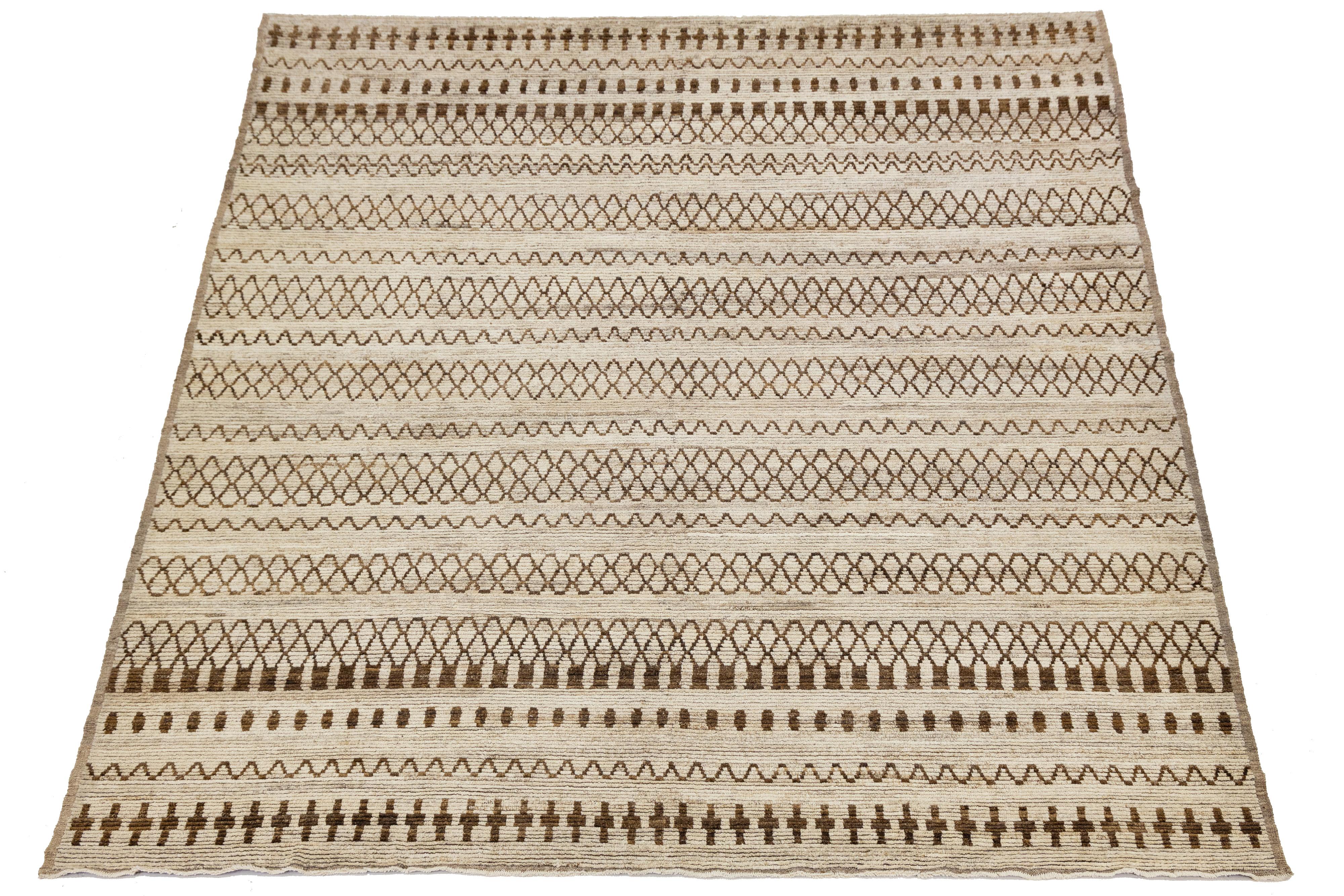 Handwoven in soft wool, this modern Moroccan-style rug features a rhythmic pattern of tribal-inspired geometric motifs in warm brown over a neutral beige field. Its minimalist palette and artisanal texture make it ideal for contemporary, bohemian,