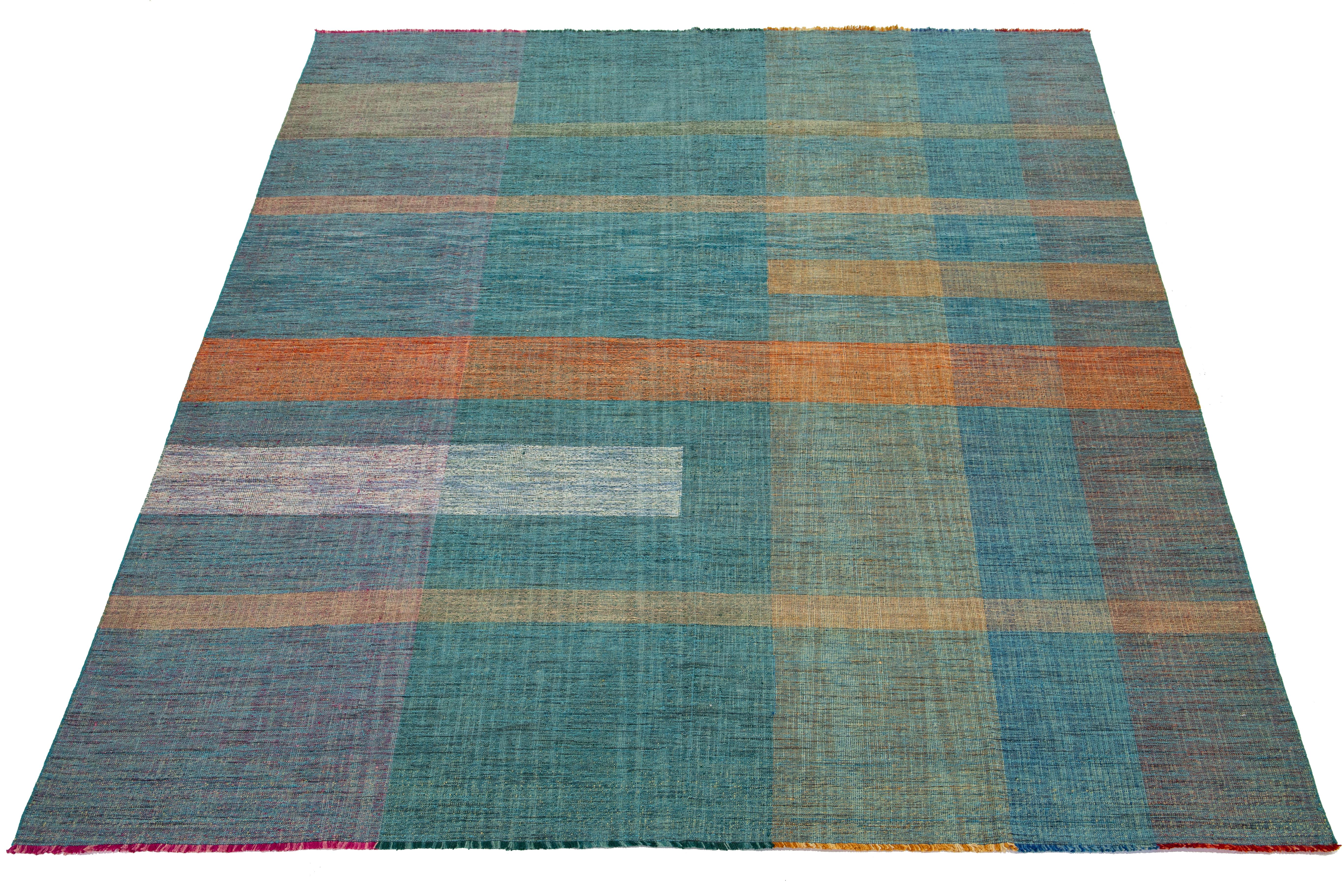 This rug showcases an organic modern design with a wool Kilim flatweave, featuring a geometric pattern in vibrant hues of teal, orange, green, blue, and pink.

This rug measures 10'1