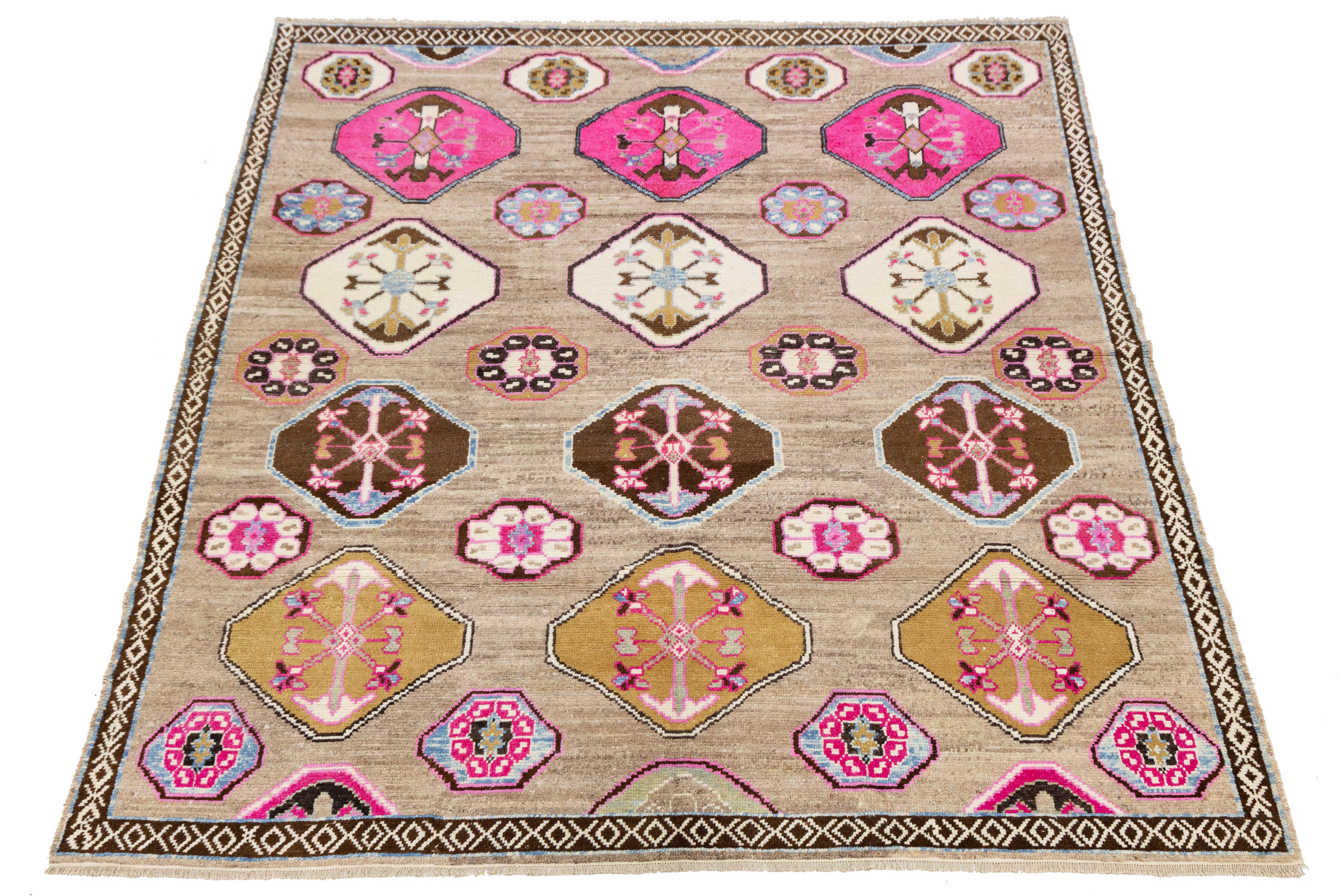 Tessuto a mano in Turchia, questo tappeto contemporaneo in lana di Kars presenta file di medaglioni esagonali e circolari con motivi floreali e geometrici in rosa, oro, blu e marrone. Su un campo neutro beige, la tavolozza vibrante è incorniciata da