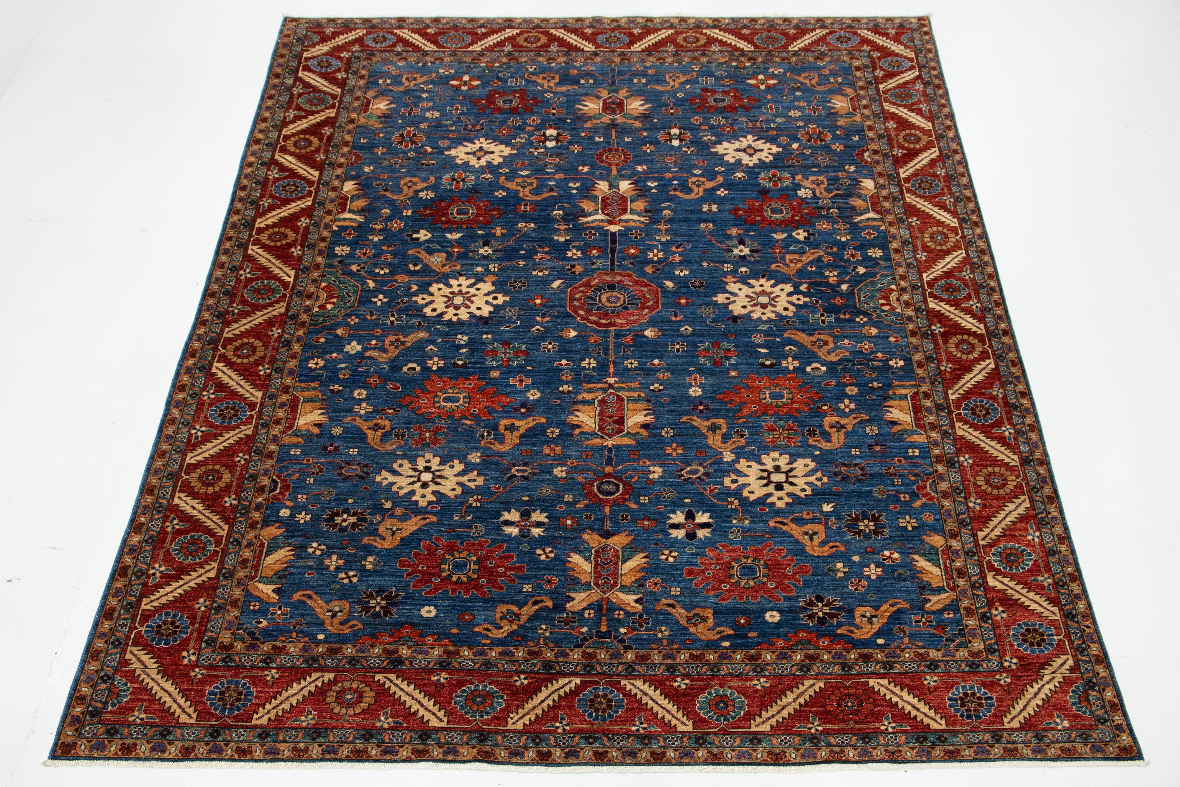 Dieser raffinierte Wollteppich zeichnet sich durch einen zeitlosen marineblauen Hintergrund aus, der mit einem modernen, von Serapi inspirierten Design kombiniert ist. Das Stück zeigt einen rot akzentuierten Rahmen und ein atemberaubendes, florales