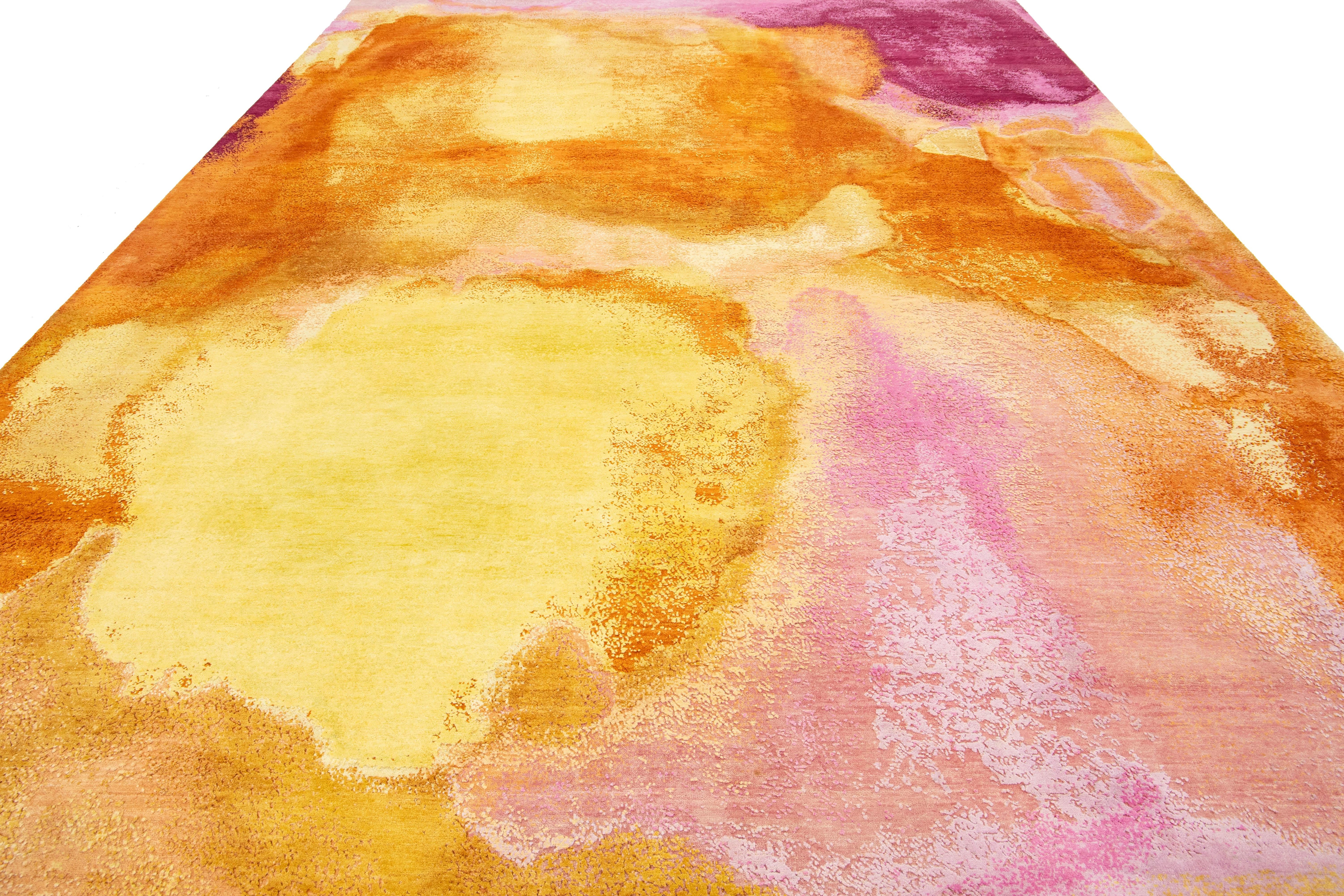 This contemporary hand-knotted rug showcases a stunning abstract design in vibrant colors that effortlessly captures attention. Made from high-quality wool or silk, it features intricate details and a rich palette of pink, ochre, and orange, adding