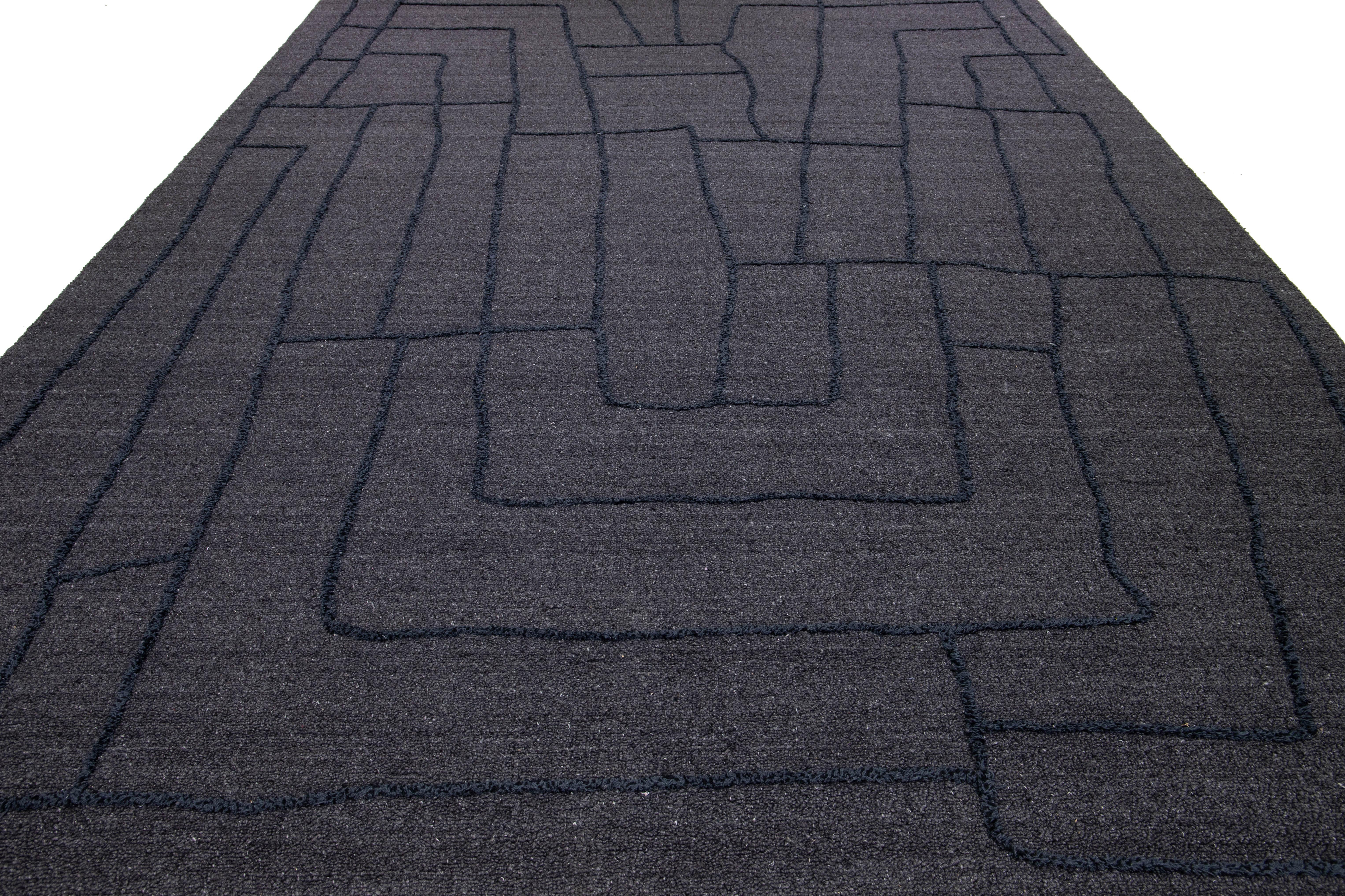 This exquisitely designed modern wool rug is bound to captivate attention. Its sophisticated gray background provides the perfect canvas for the intricate abstract pattern in navy blue hues. This striking visual contrast infuses depth and