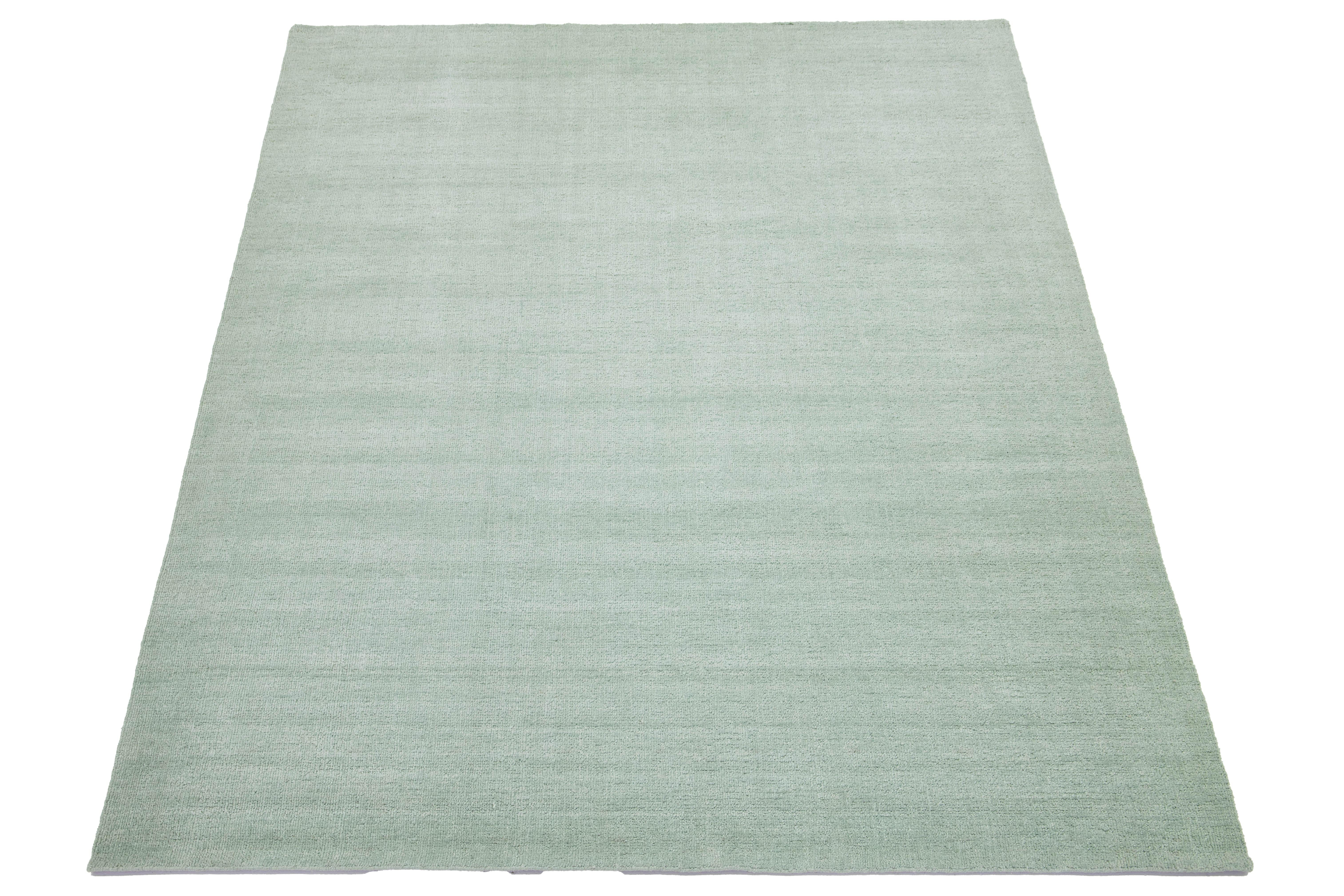 Esta alfombra india contemporánea de lana anudada a mano ha sido cuidadosamente elaborada por hábiles artesanos y presenta un diseño minimalista. Su suave color verde claro actúa como base versátil, complementando sin esfuerzo una gama de estilos de