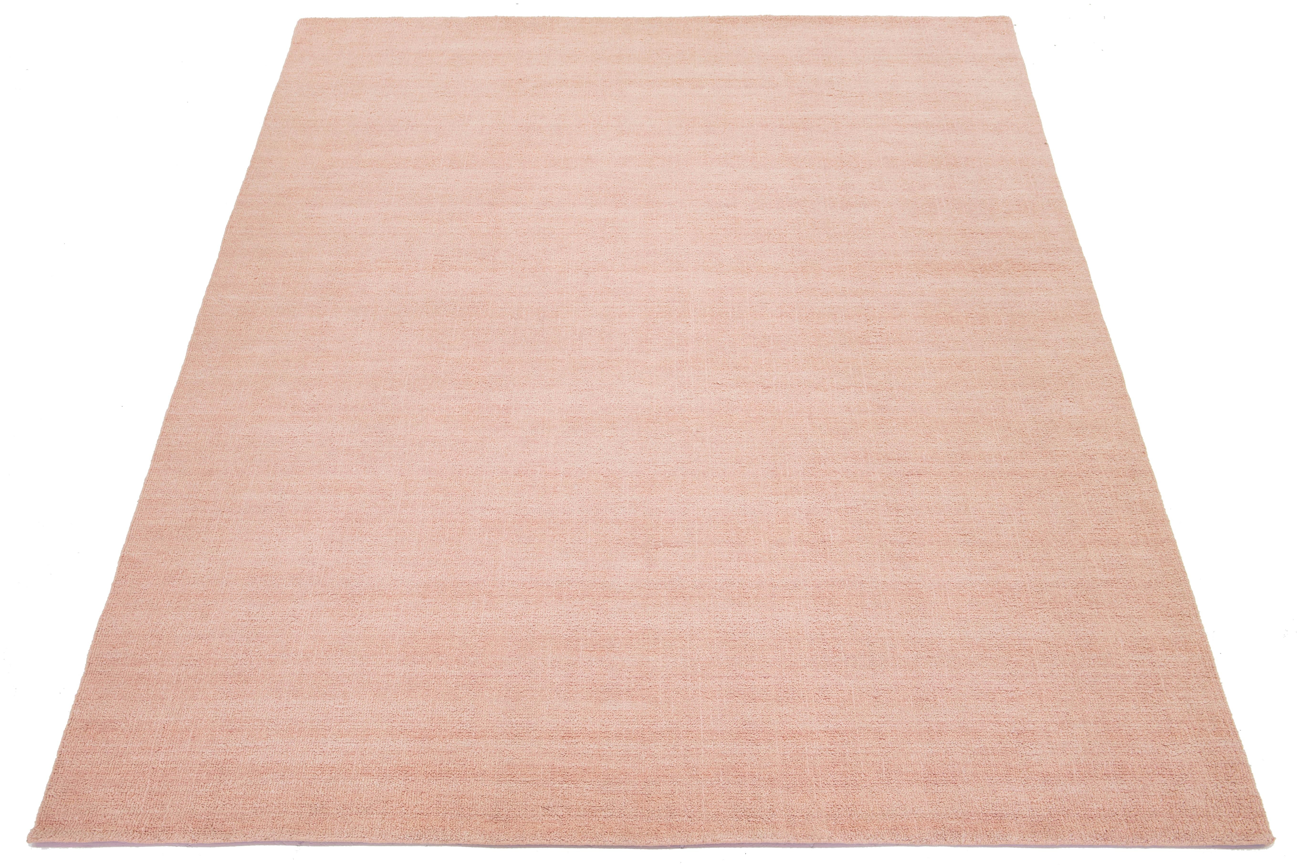 Questo moderno tappeto indiano in lana annodato a mano è abilmente tessuto da artigiani e presenta un design solido. La sua tonalità rosa tenue funge da sfondo versatile, consentendole di integrarsi perfettamente con vari stili di interni, da quelli