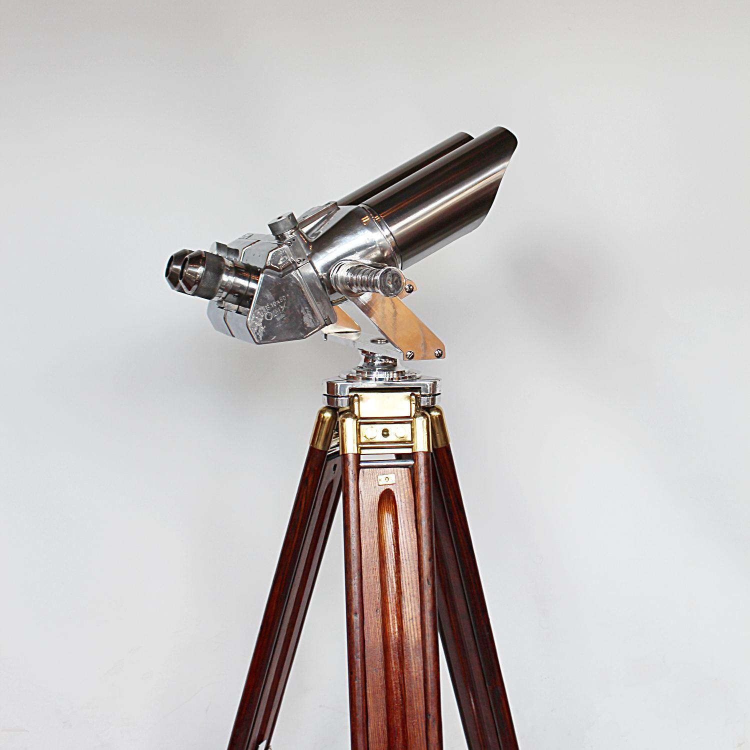 A pair of 10 x 80 binoculars with eyeglasses set at 45 degrees, attributed to Zeiss. Set on period, extending oak and brass stand with chromed, conical feet. 10 times magnification with 80mm objective lens.

Paint stripped and metal polished.