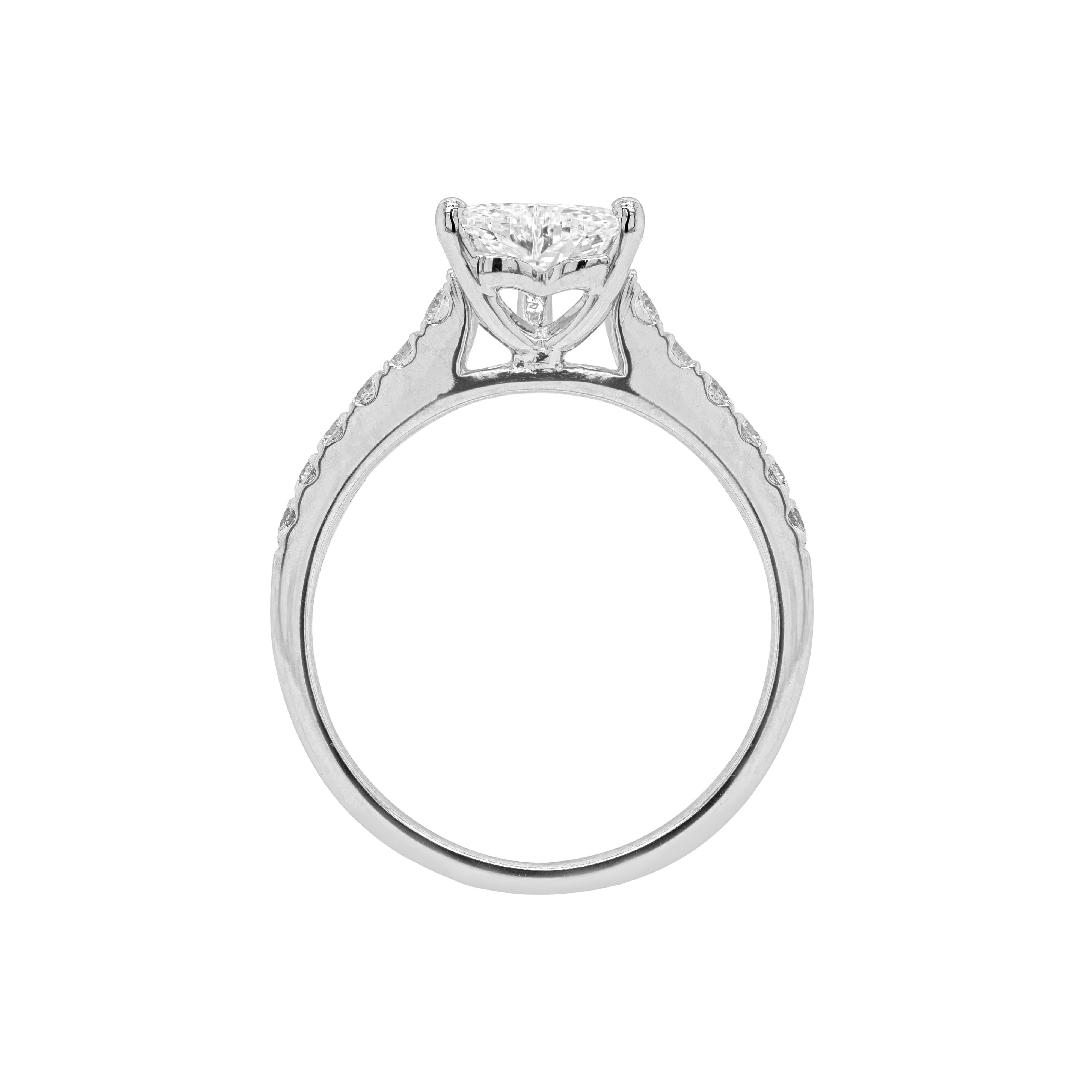Cette bague de fiançailles exquise présente un merveilleux diamant en forme de cœur de 1,00ct, de couleur I et de pureté VVS1, monté dans une monture ouverte à trois griffes. La belle pierre est accompagnée de six beaux diamants ronds de taille