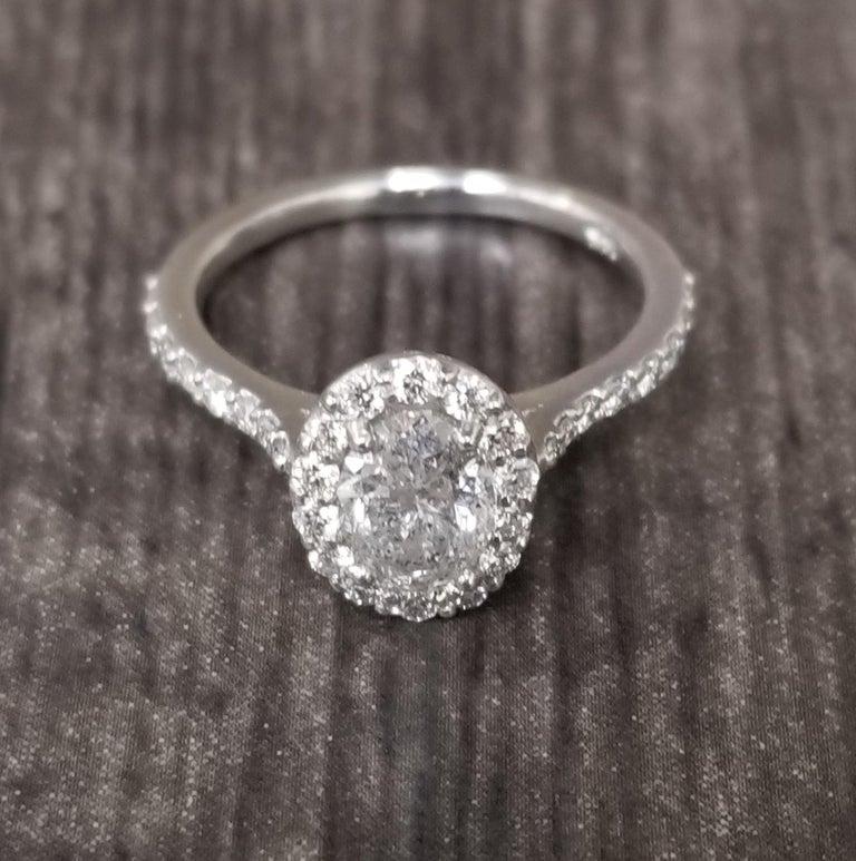 14k white gold ladies diamond ring containing 1 oval cut diamond weighing 1.00cts. and 20 round full cut diamonds of very fine quality weighing .45pts. set in a halo style setting.