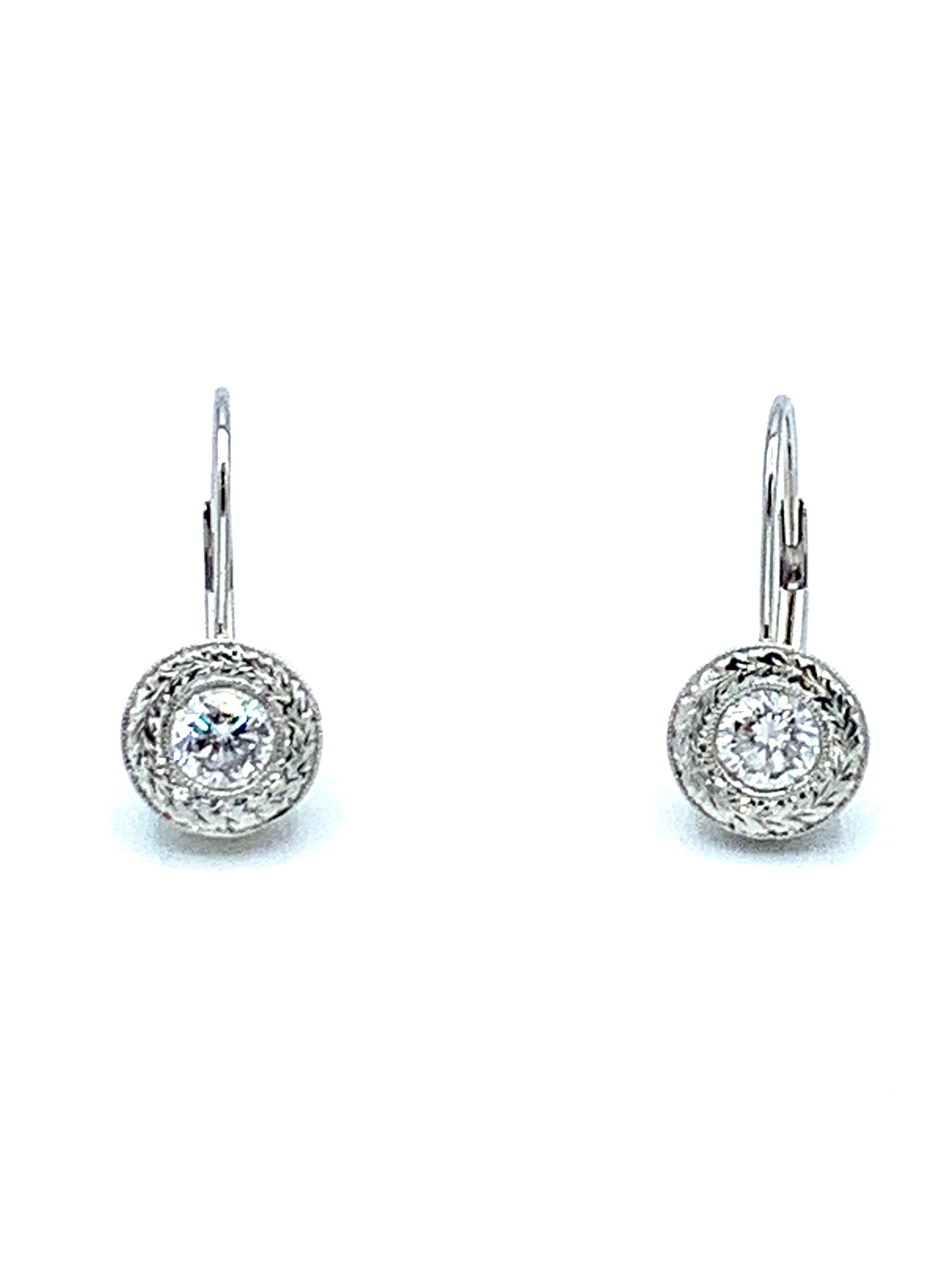 A gorgeous easy to wear pair of earrings!  The 1.00 carat total weight diamonds are bezel set, surrounded by hand engraved metal work, suspended from a curved lever back closure in platinum.  The diamonds are round brilliant cuts, graded as F color,