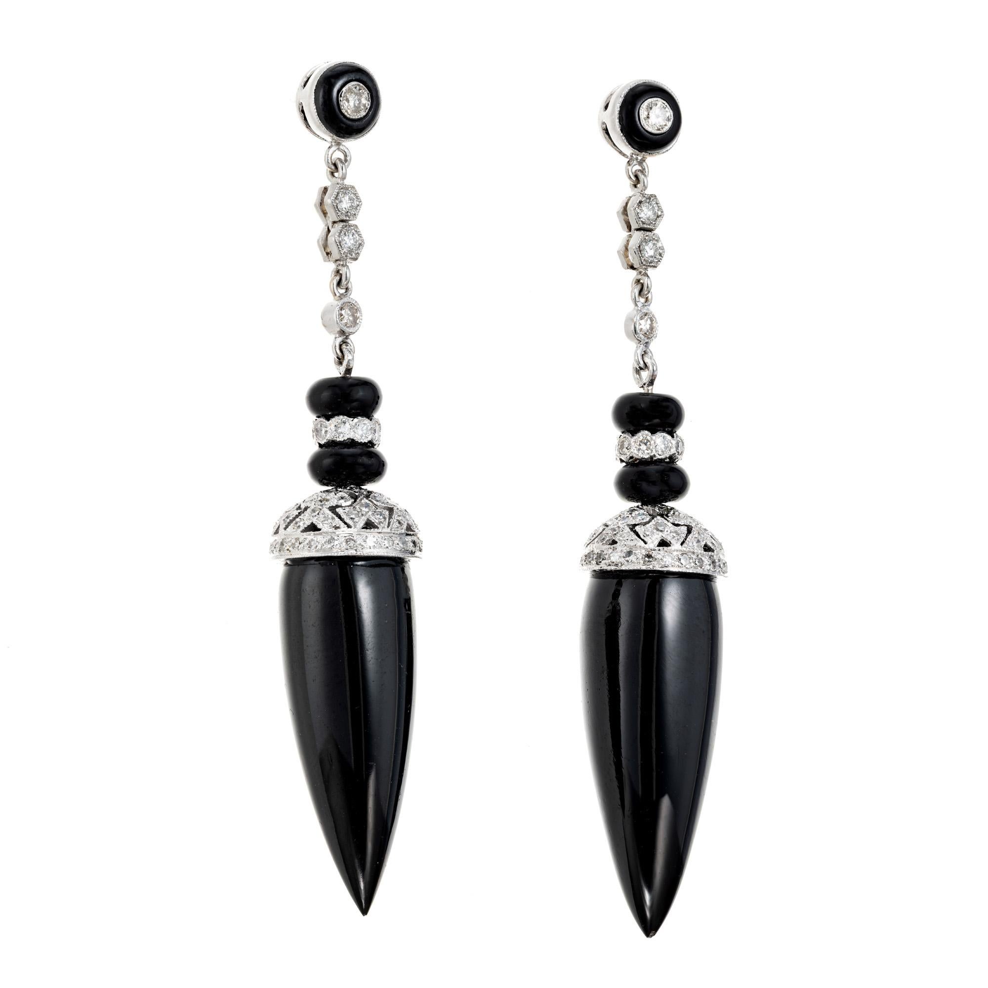 Dramatic 1970's onyx and diamond dangle drop earrings. 2 black upside down tear dop shaped onyx, each one is capped with a white gold filigree pave diamond tops, connected to the post by a chain of round bezel set diamonds, separated by circular