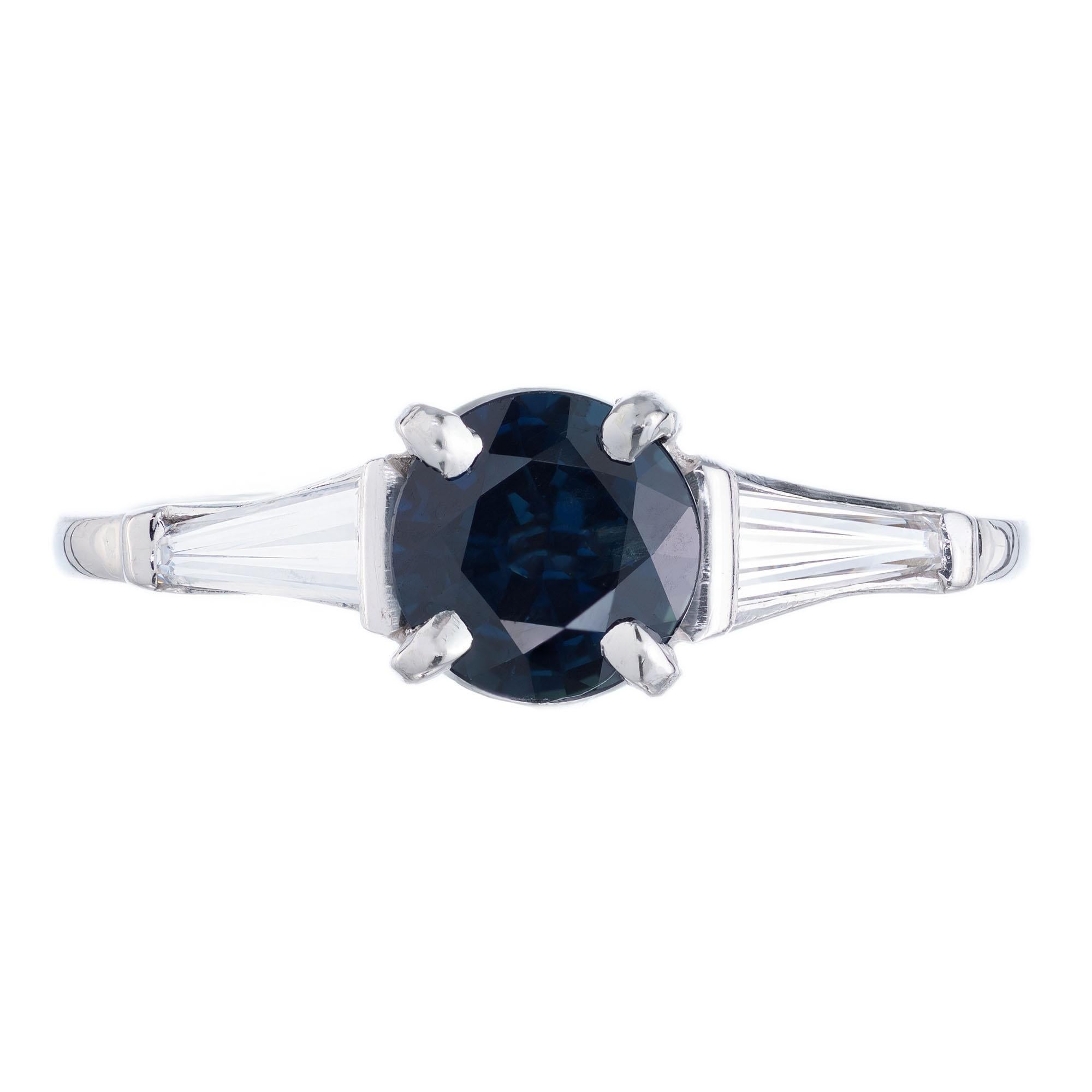 1.00ct round Royal blue Sapphire in a classic three-stone platinum setting with 2 baguette side diamonds. 

1 round deep Royal blue Sapphire, approx. total weight 1.00cts, 5.9mm, simple heat only
2 tapered baguette diamonds, approx. total weight