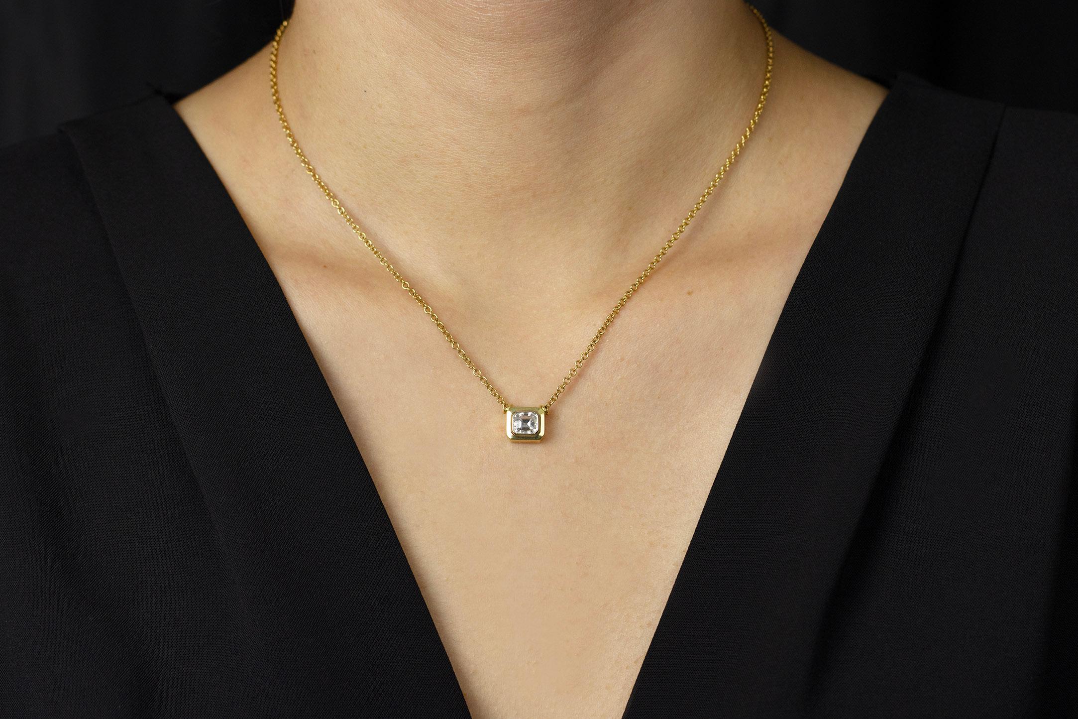 A simple yet versatile pendant necklace showcasing an emerald cut diamond approximately weighing 1.00 carat, bezel set in a horizontal manner. Bezel made in 18k yellow gold. Attached to an 18 inch adjustable yellow gold chain.

Style available in