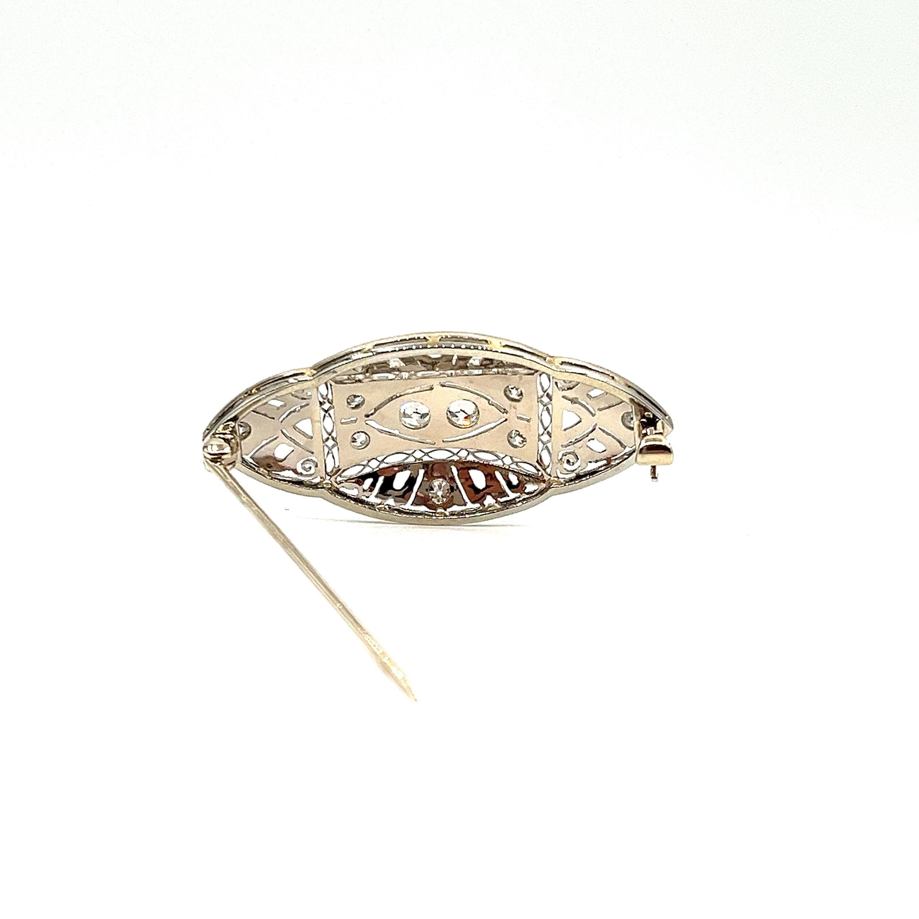 This exquisite brooch showcases approximately 1.00 carat round diamond with VS2 clarity and F color grade. Set in a blend of platinum, and 18k white gold, the intricate design highlights the Art Deco style. Measuring 1.62 inches in length and 0.75