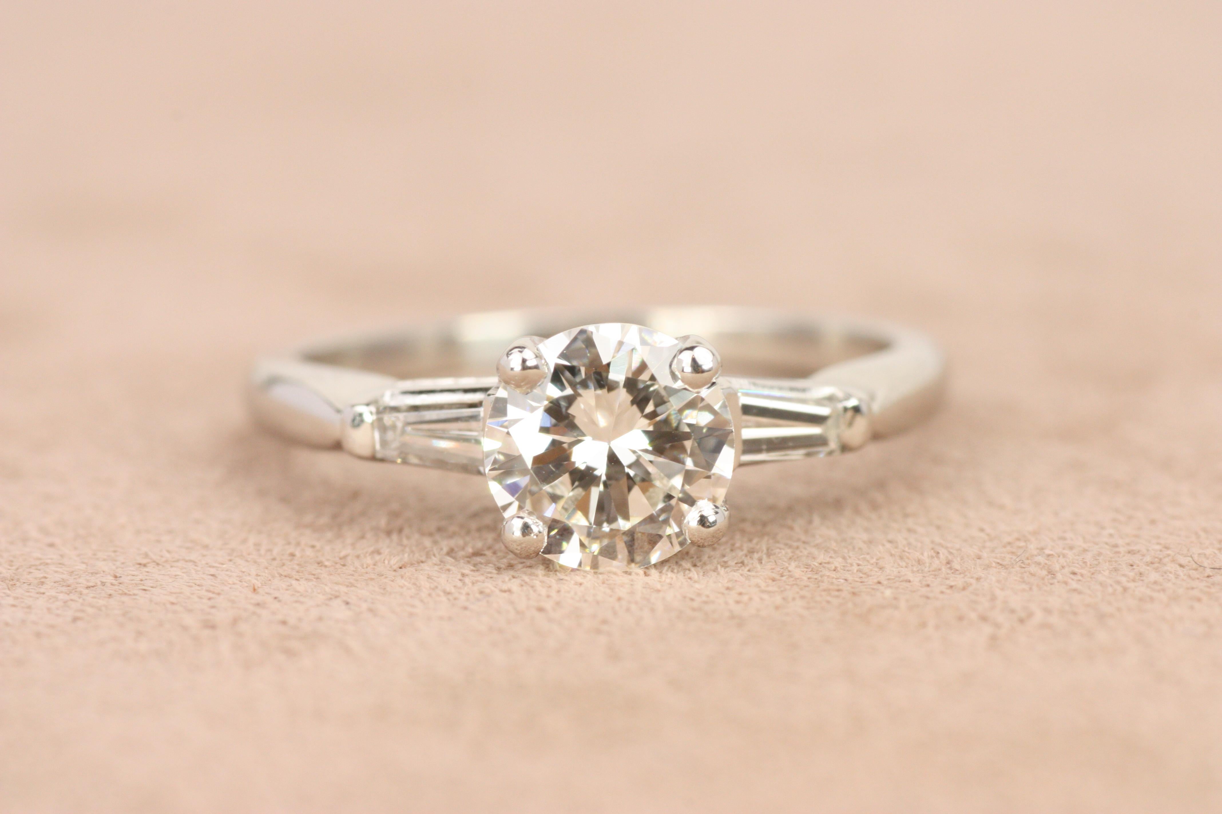 Inspirée du design des années 1950, cette bague de fiançailles à trois pierres en platine présente un diamant rond de 0,82ct de taille brillante flanqué de deux diamants baguettes effilés. L'élégance classique de la bague et son éclat intemporel en