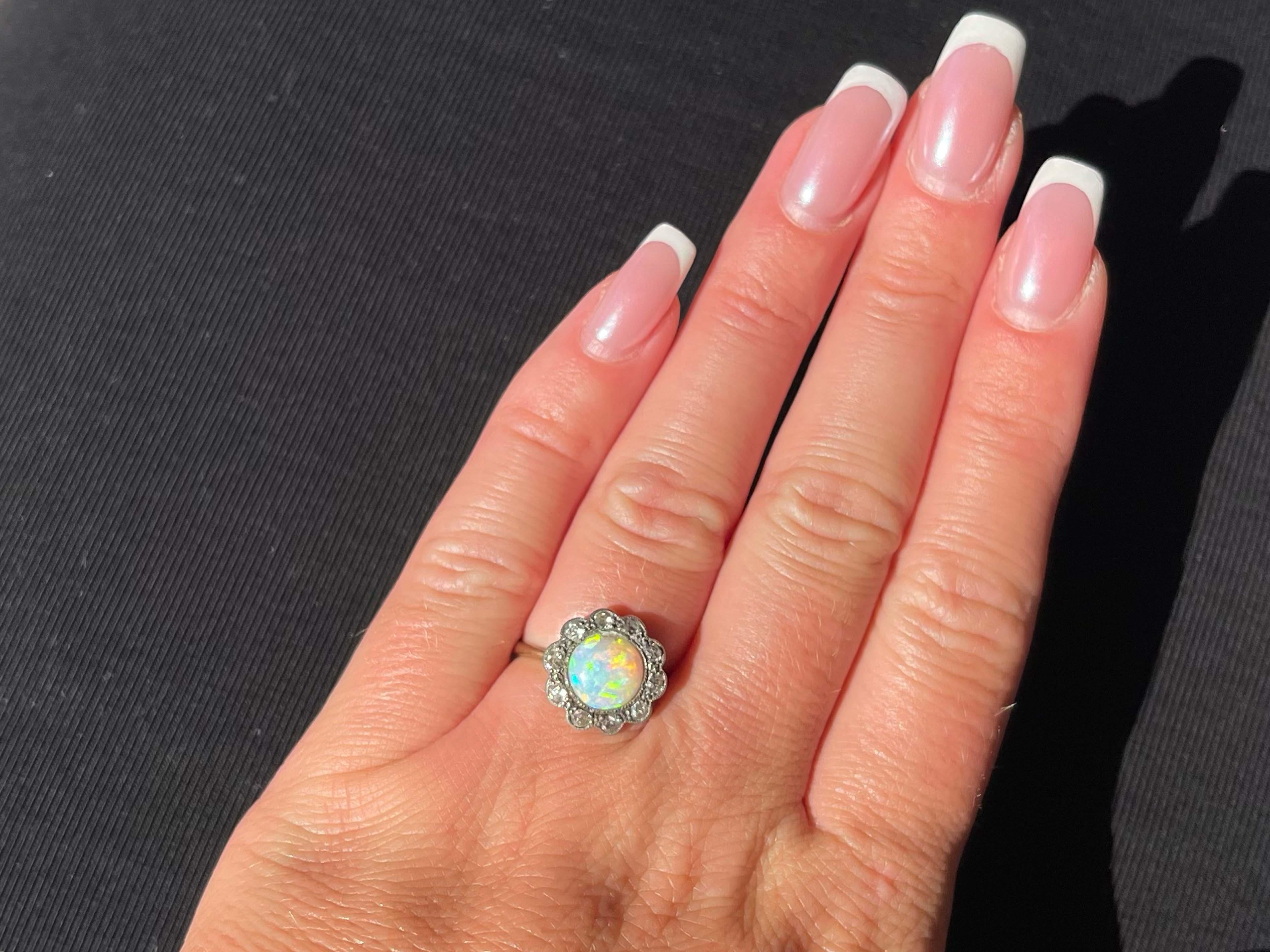 This antique ring was made during the beginning of the 1900's and is estimated to be over 100 years old. It features a stunning opal with beautiful yellow orange and blue hues. Around the opal are 10 old European cut diamonds making a flower halo.