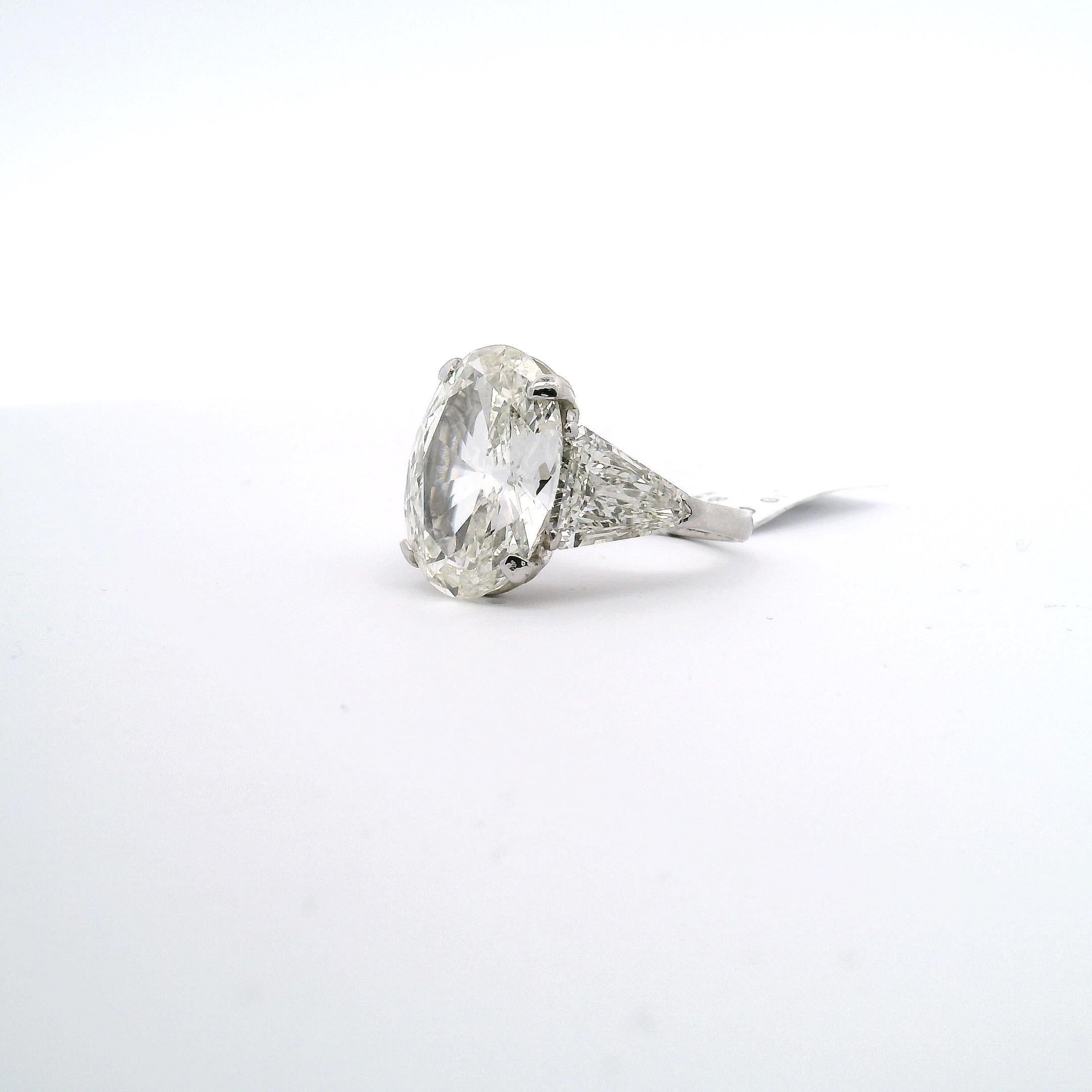 Traditional style engagement ring with 10.02ct. oval diamond and two triangle shape side diamonds.

Center diamond approximately 10.02ct. 
Clarity grade is SI2 
Color grade is K
Dimensions are 18.20 x 13 x 6.02mm
 
Side diamonds approximately