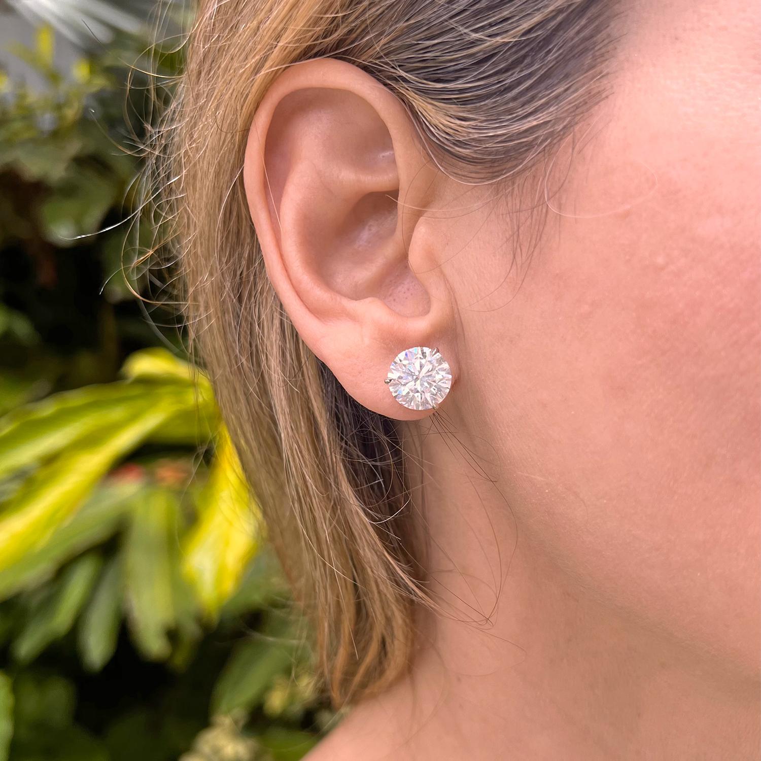 Round brilliant cut diamond stud earrings, showcasing a pair of well-matched colorless diamonds weighing 10.09 total carats, the diamonds secured in three-prong platinum martini settings with posts for pierced ears. Both diamonds are D-color and