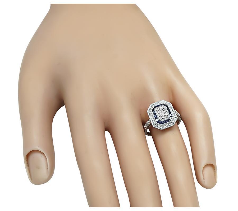 This is a stunning platinum engagement ring inspired from the Art Deco era. The ring is centered with sparkling emerald cut diamond that weighs approximately 1.00ct. The color of the diamond is H-I with SI1 clarity. The center diamond is accentuated