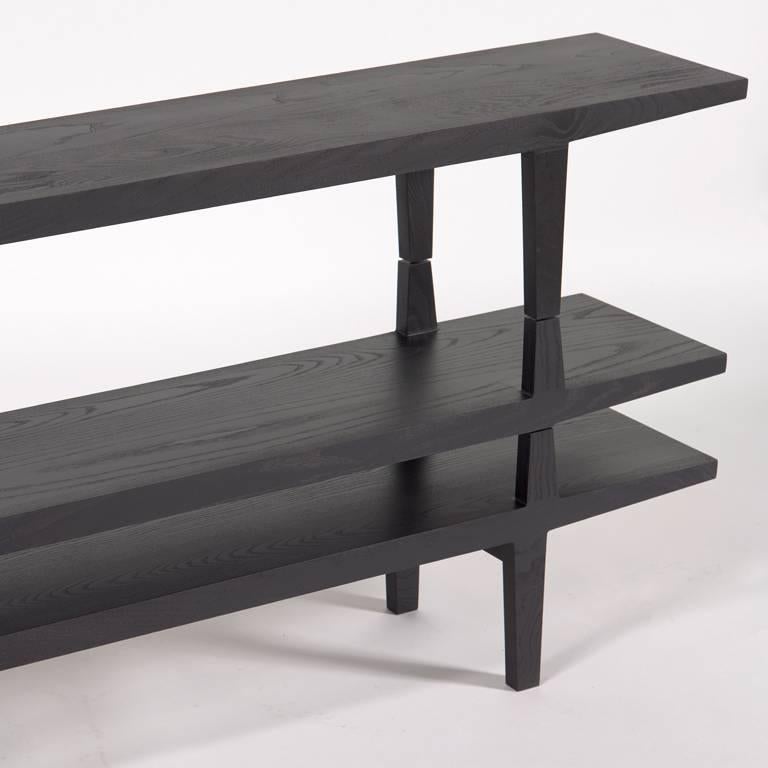 A stack-able modular shelving system consisting of three black dyed tiers in solid ash. Can be customized with more shelves or different widths.