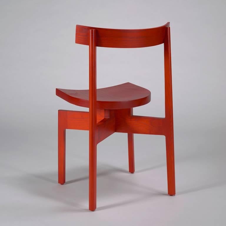 An elevated dining chair with an architectural form in red dyed ash. The Stoolback is wonderfully versatile and stacks for a smaller footprint when not in use.