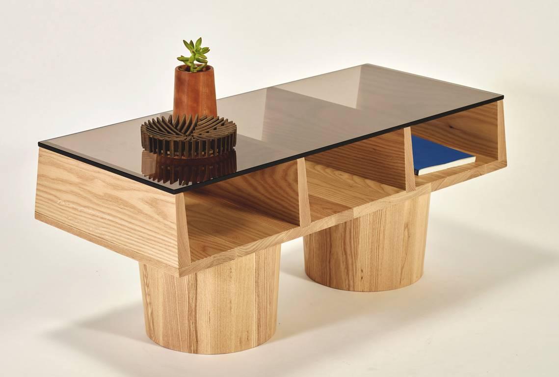 A sculptural coffee table in solid ash with integrated storage. The perfect way to display your favorite pieces of print just below the bronze glass top. The forms and proportions of this piece were inspired by the brutalist architecture of Paul