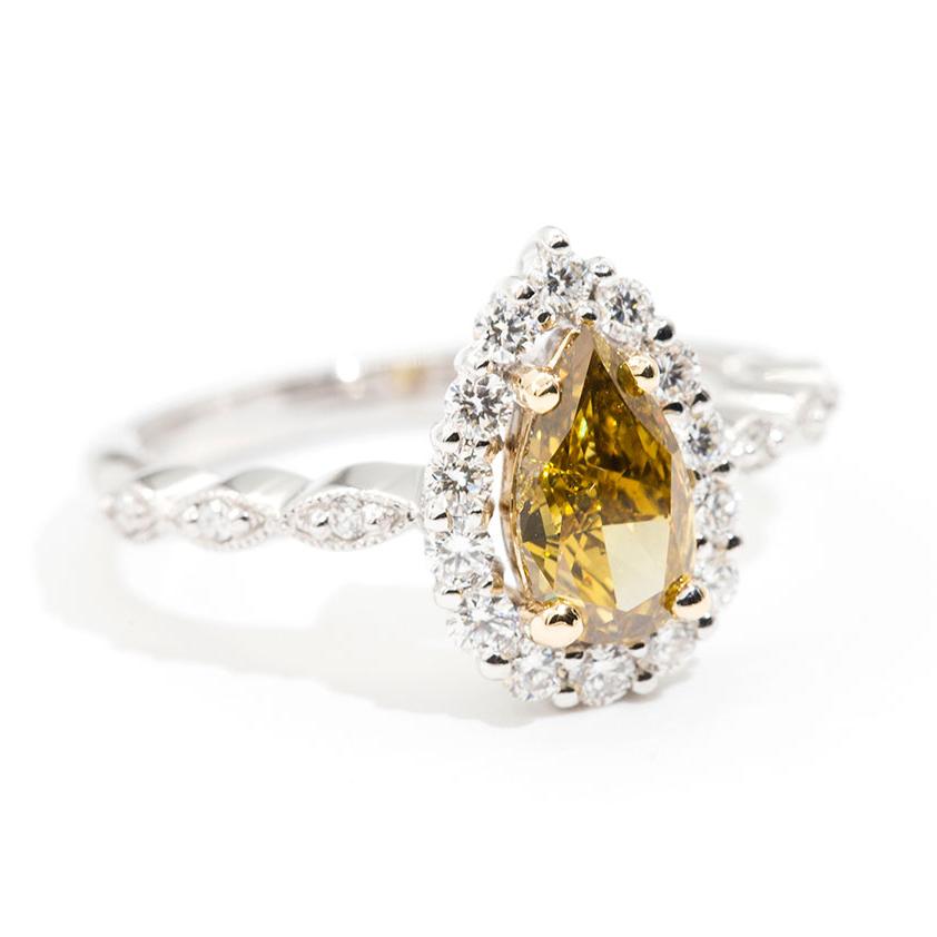 Forged in 18 carat white gold is this vintage inspired halo cluster ring featuring a sparkling certified 1.01 carat fancy intense yellow pear shape diamond encompassed by a glittering border of round brilliant cut diamonds that gracefully scallop