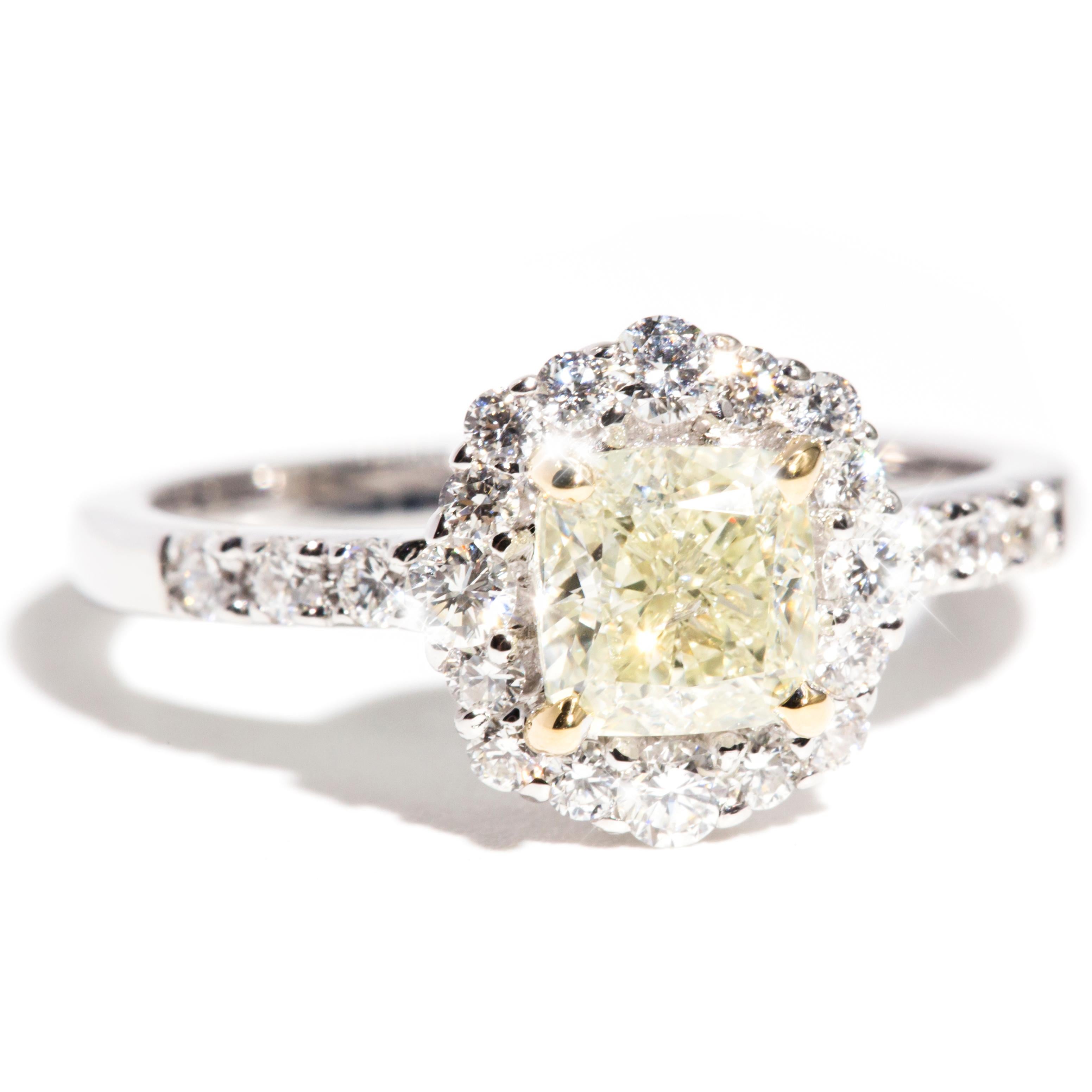 Forged in 18 carat gold is this uniquely designed contemporary engagement ring featuring an enchanting 1.01 carat certified fancy light yellow cushion cut diamond, embellished with over half a carat of glittering white round brilliant cut diamonds.