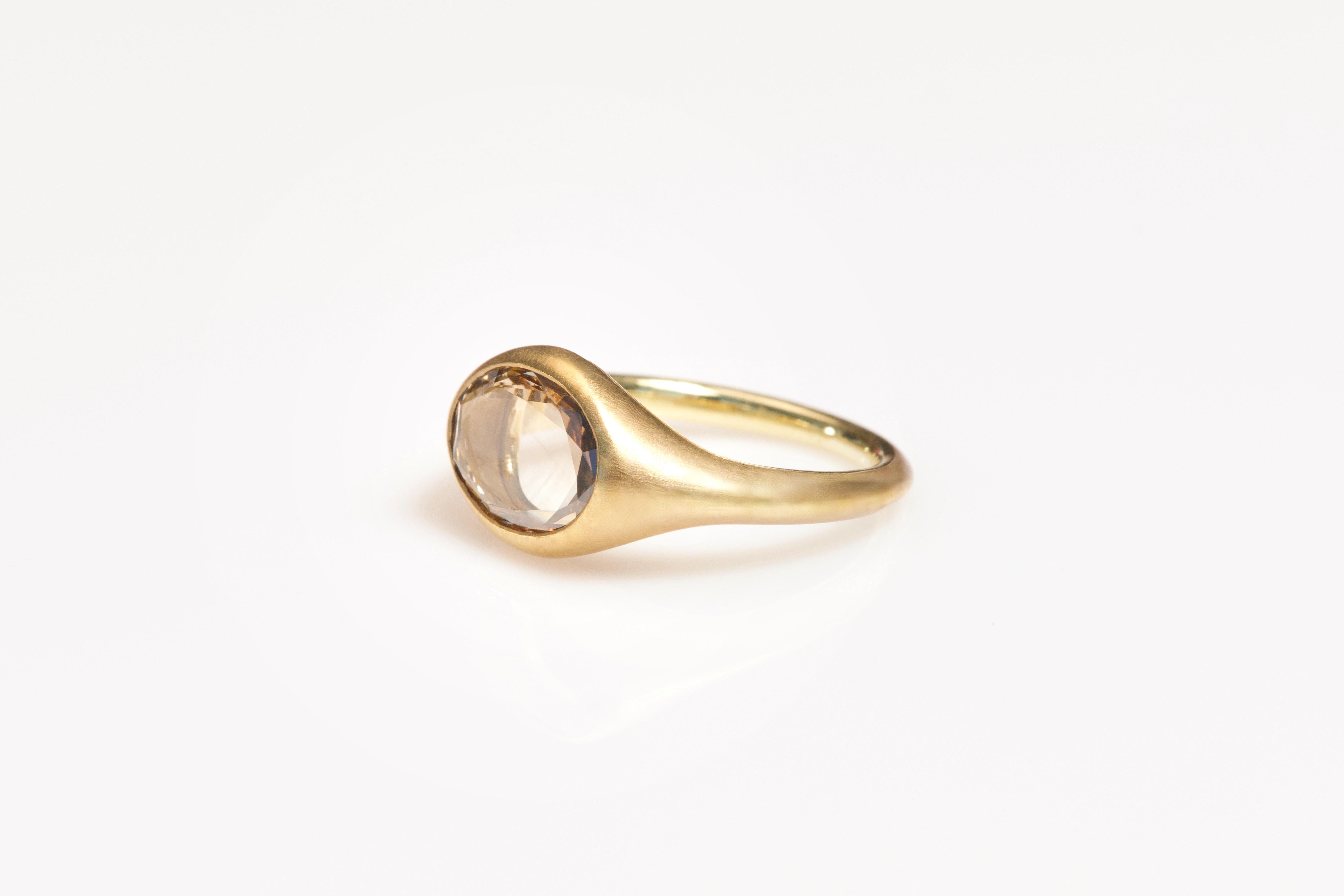 This elegant ring features a 1.01ct oval portrait-cut light brown diamond, bezel-set for a sleek, refined look. The bronze setting enhances the diamond’s soft, warm glow, while the 18k yellow gold shank adds a luxurious contrast. A unique blend of