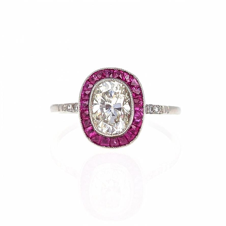 This stunning engagement ring centers upon a 1.02 carat cushion-cut diamond with SI clarity and I/J color. It is surrounded by vibrant calibre-cut rubies and further accented by three round-cut diamonds on each side. The head is low in profile and