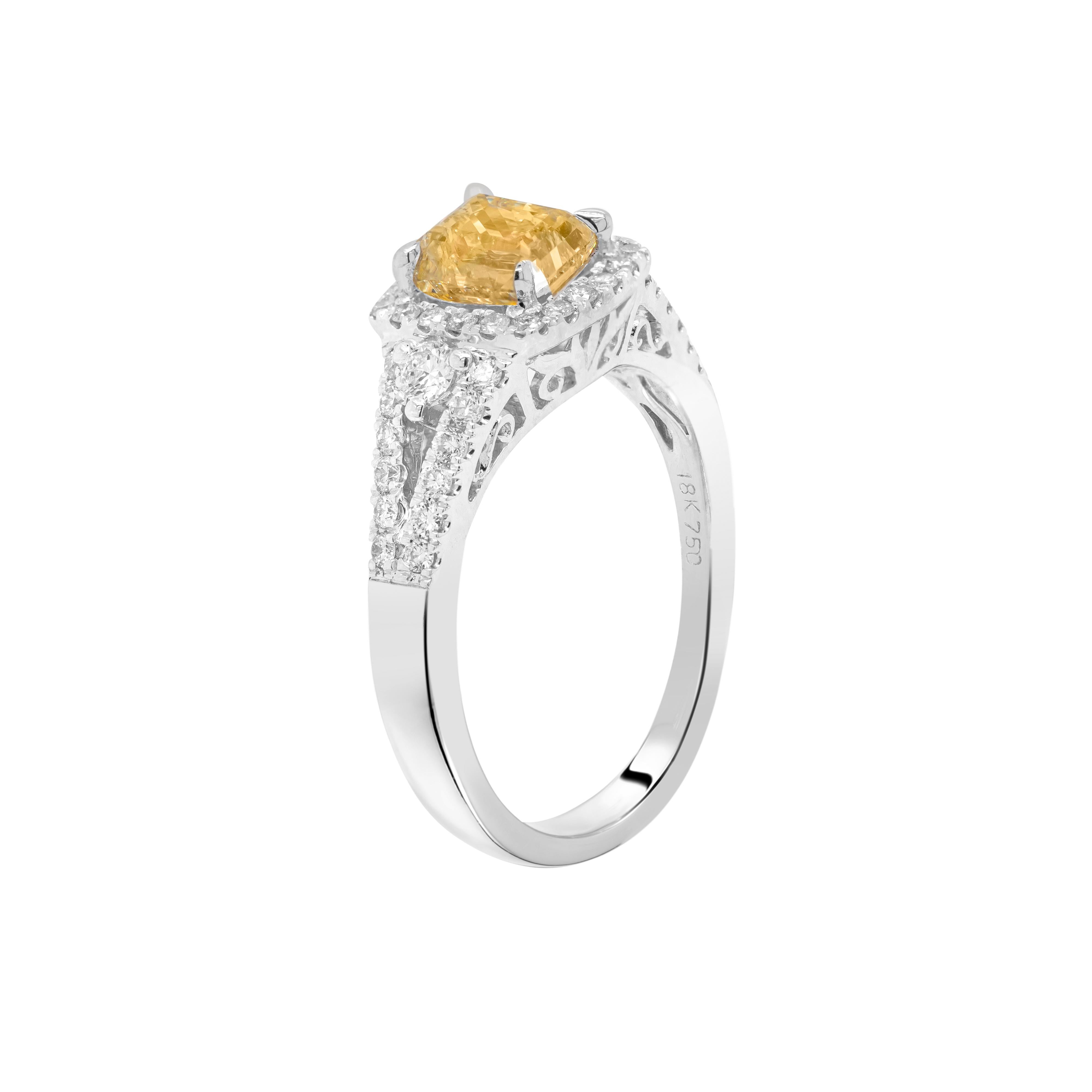 This wonderful 18 carat white gold engagement ring features a beautiful 'variation emerald cut' shaped fancy yellow diamond weighing 1.02ct, mounted in a four claw, open back setting. The exquisite stone is surrounded by a halo of fine round