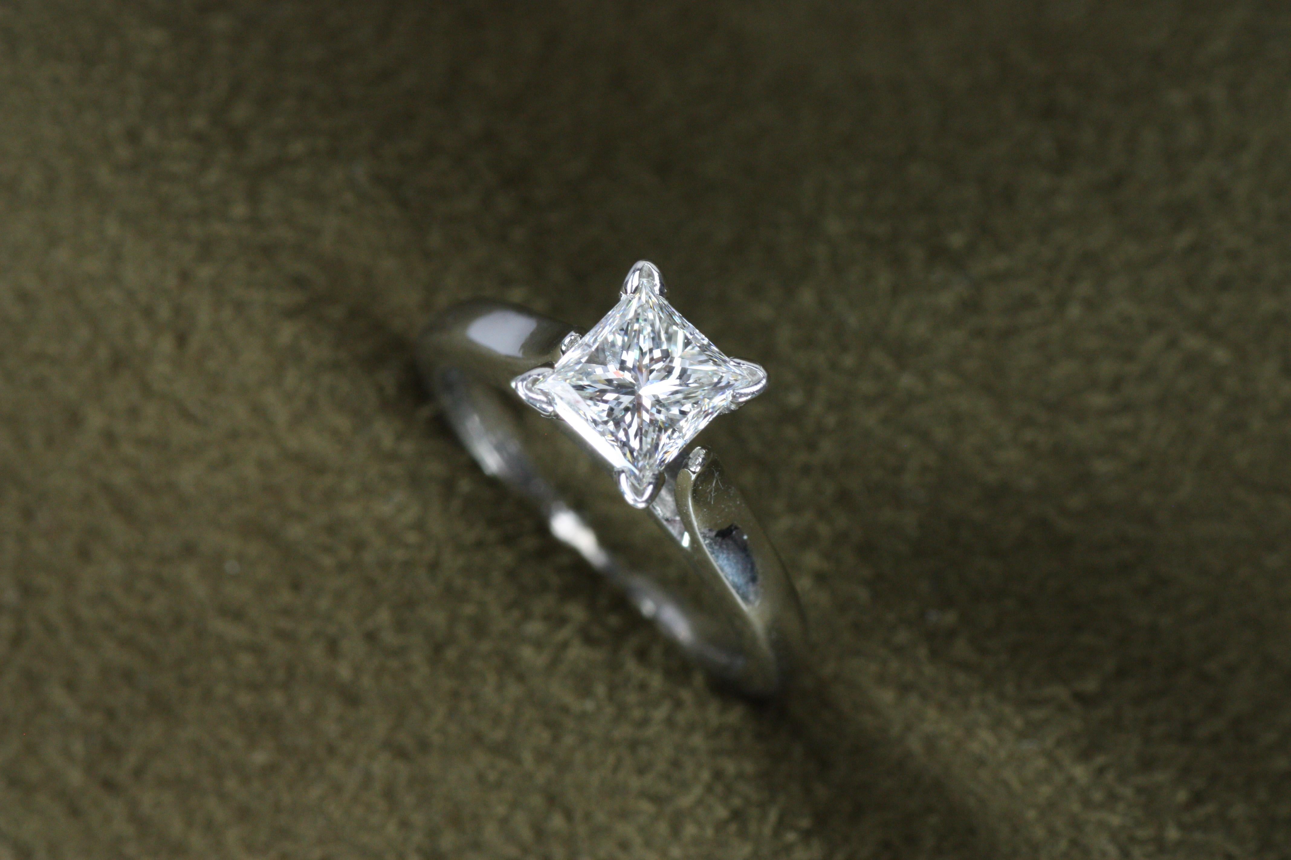 Une bague de fiançailles solitaire chic et moderne, avec un diamant de taille princesse de 1,02 carat serti dans un anneau de platine étincelant. Son design épuré et élégant en fait un choix intemporel pour les romantiques modernes et le détail