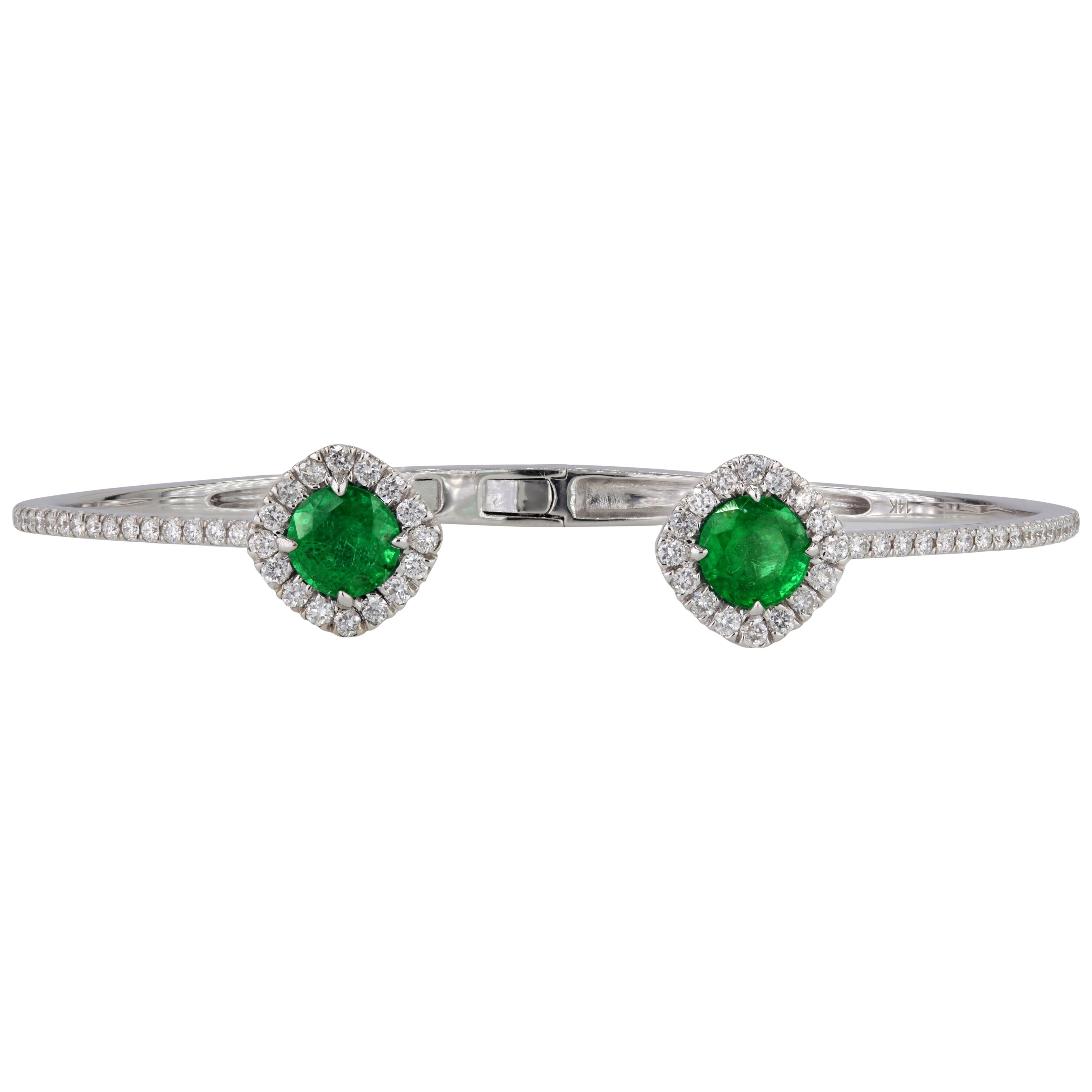 This bangle features two round-cut emeralds at its focal points, elegantly encircled by a closely set halo of round white diamonds that extends to the midpoint of the bangle. The arrangement of the halo cleverly creates the illusion of a cushion-cut
