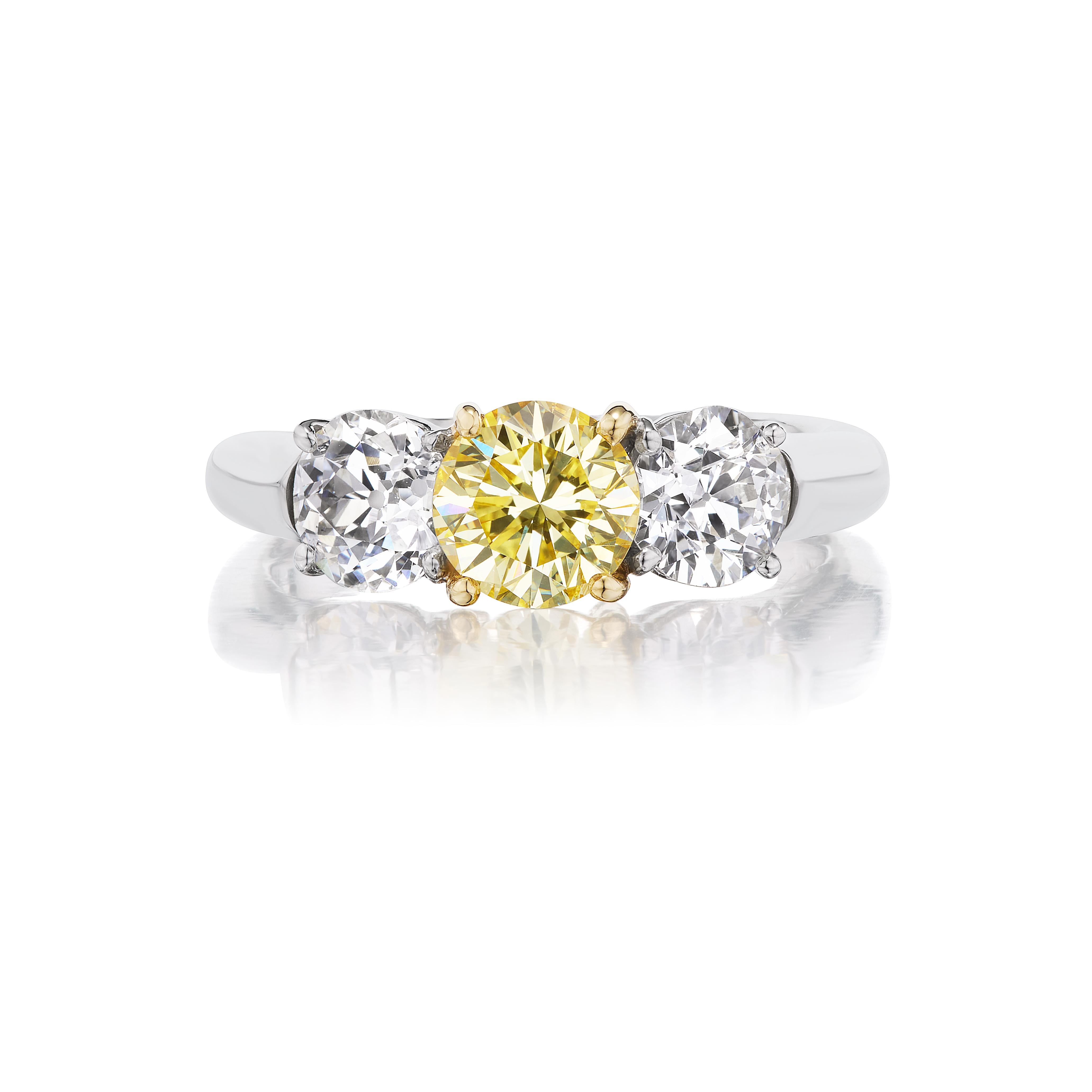 This very sweet 3 stone ring features a 1.02 round brilliant fancy light yellow VS1 clarity center diamond accompanied by a .68 and .75 carat old mine cut white diamond to either side. Round brilliant is an exceedingly rare shape for fancy color