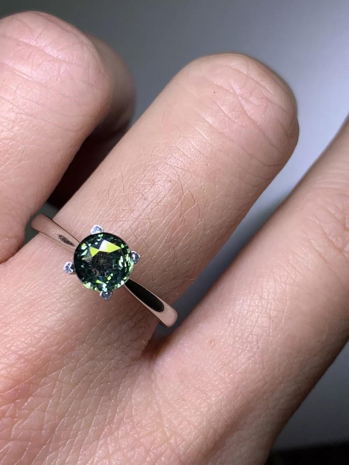 This stunning engagement ring features a 1.02ct round teal sapphire set in 18ct white gold. The solitaire setting style showcases the natural beauty of the gemstone. The ring is size M 1/2 and is perfect for any special occasion. Crafted with fine